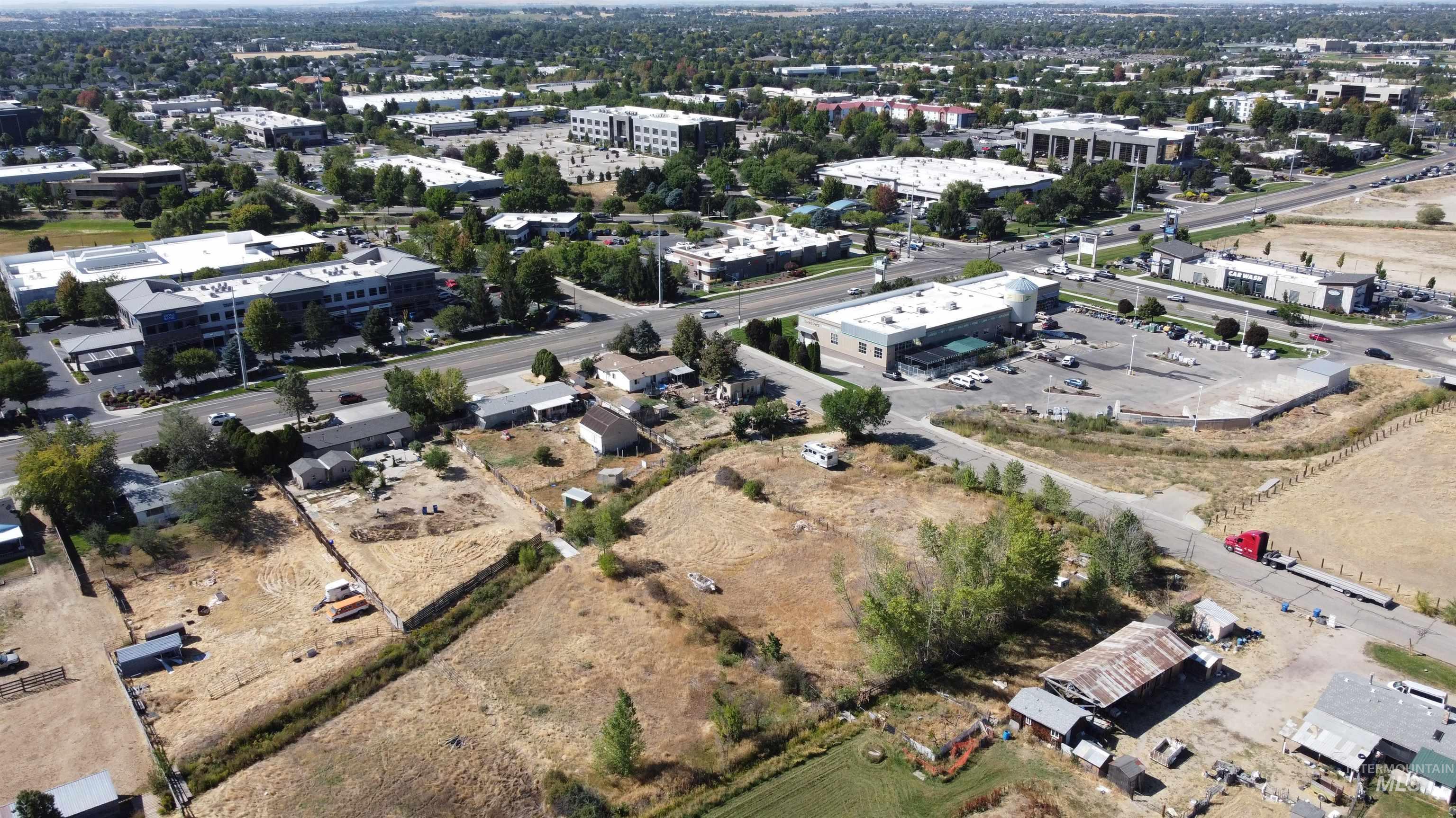 Aerial view of dry, partly cleared land beside a major road and commercial buildings.