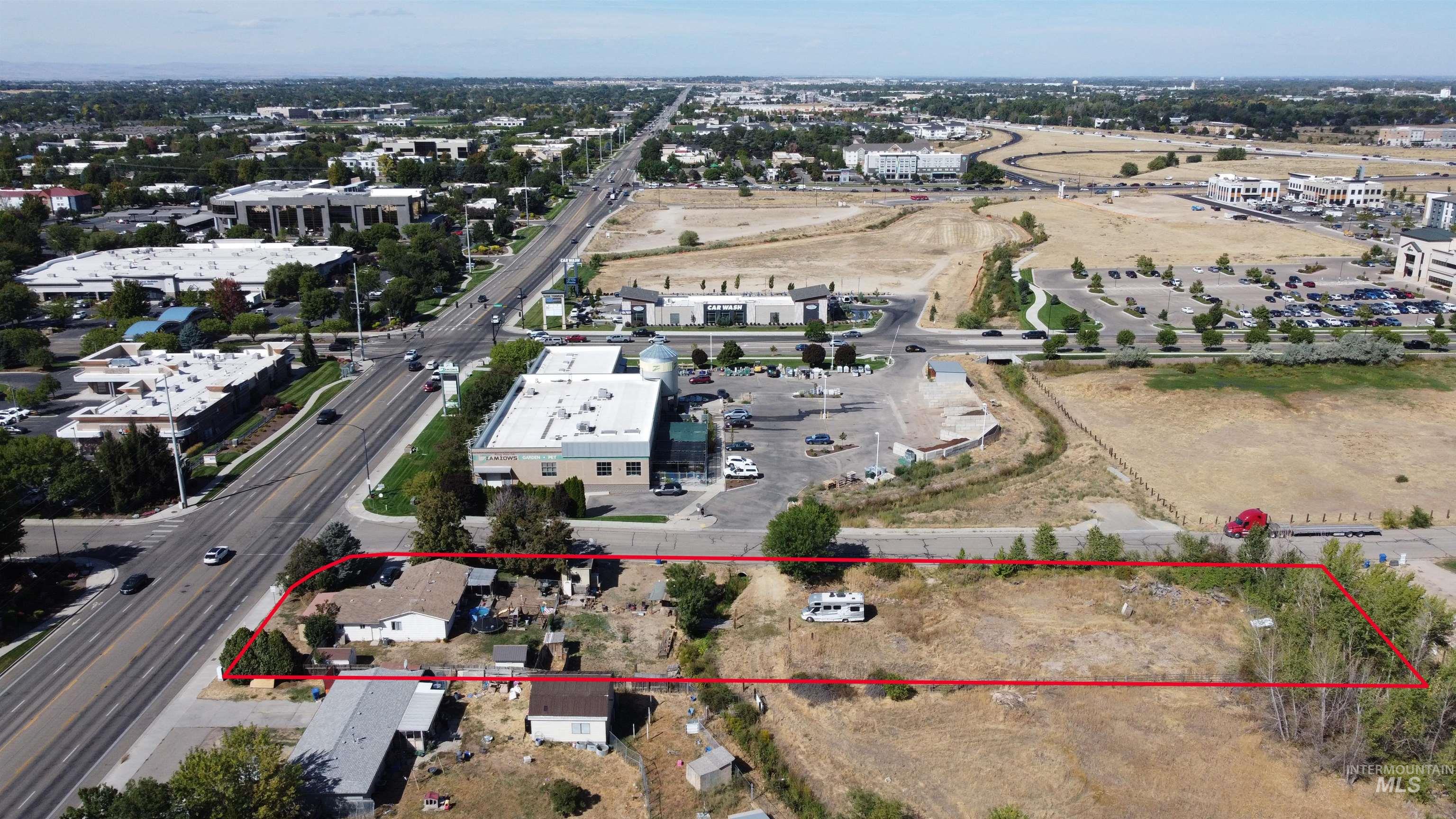 Aerial view of a mostly undeveloped parcel outlined in red beside a major road.