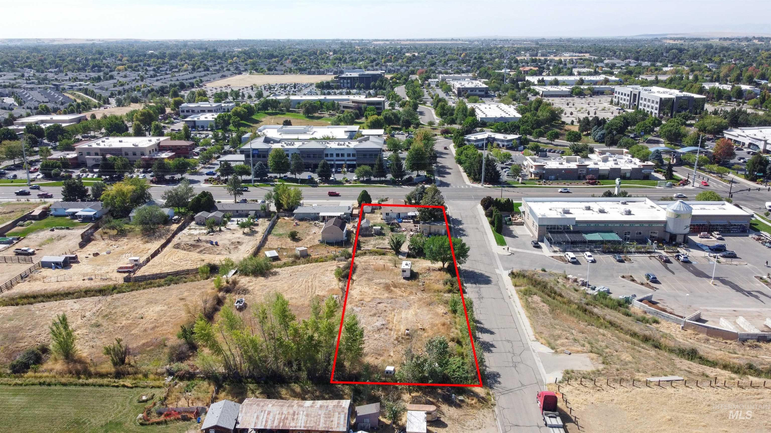 Aerial view of a mostly open parcel outlined in red beside a road and commercial buildings.