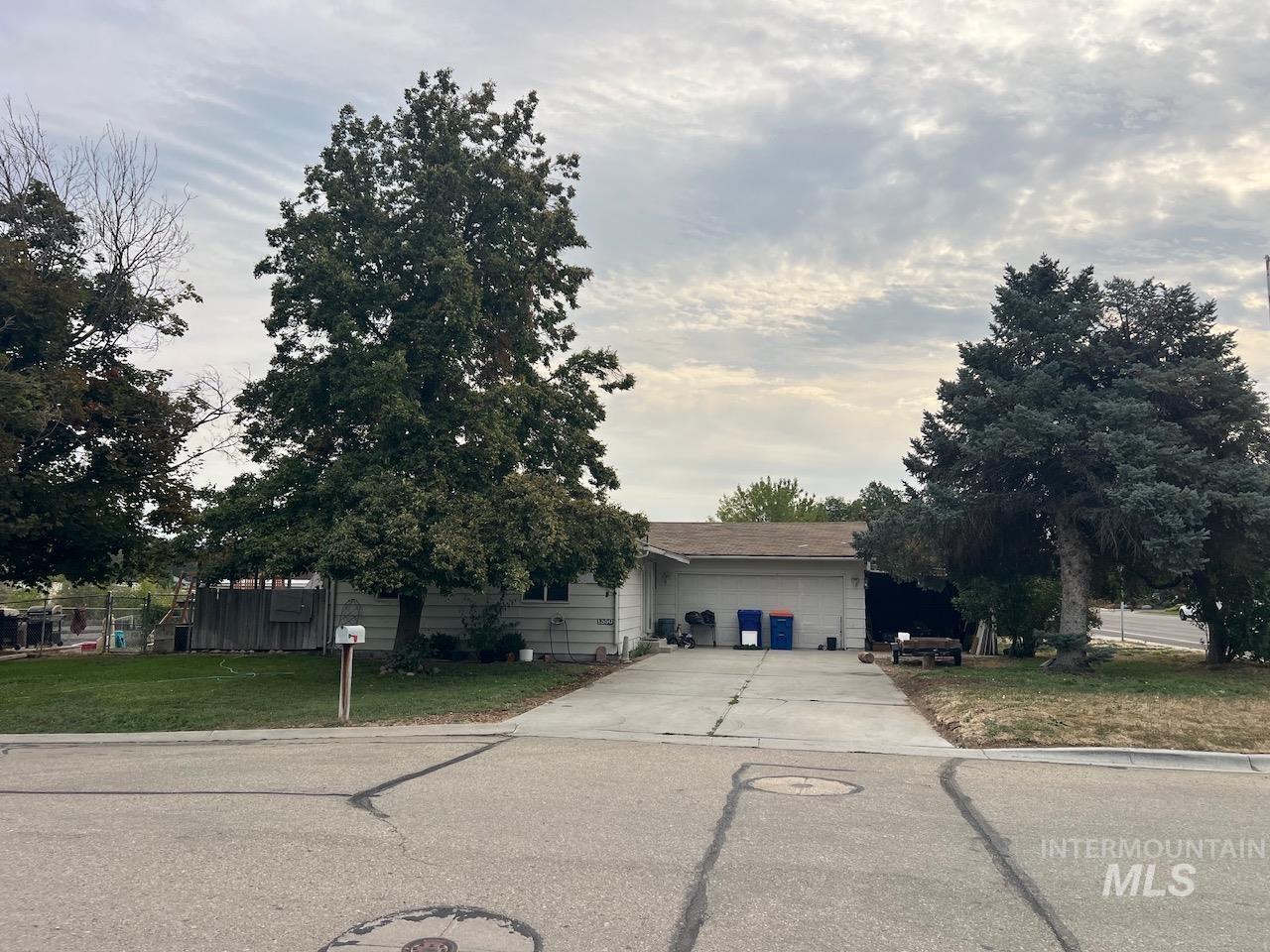 Single-story house partly shaded by mature trees, with a wide driveway leading to the attached garage.