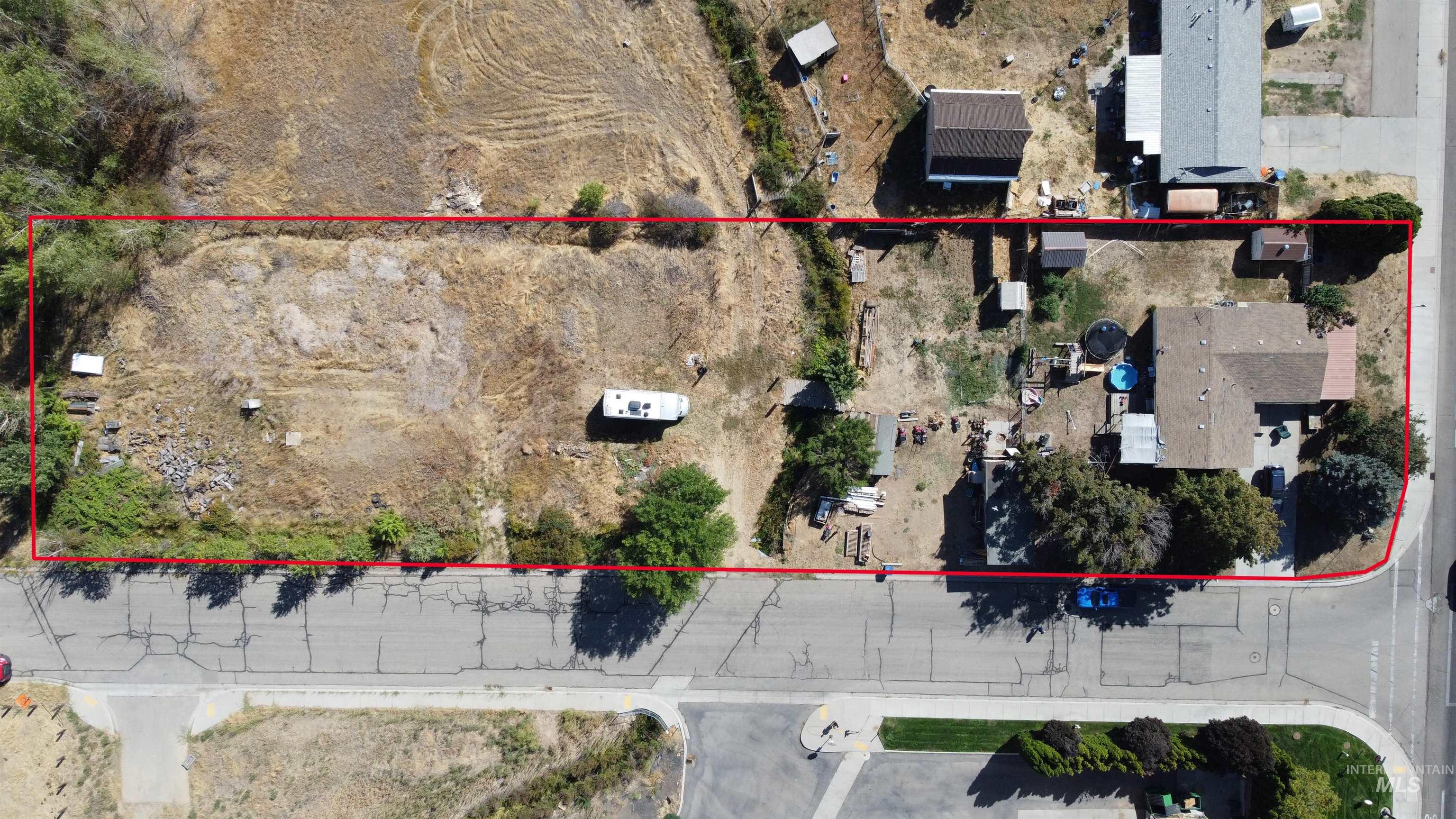 Aerial view of a red-outlined parcel with a house and yard beside a large open area.