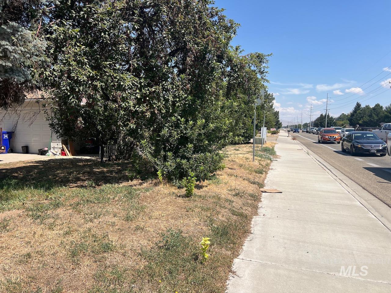 Property frontage with dense shrubs, a partly visible garage, and a sidewalk beside the road.