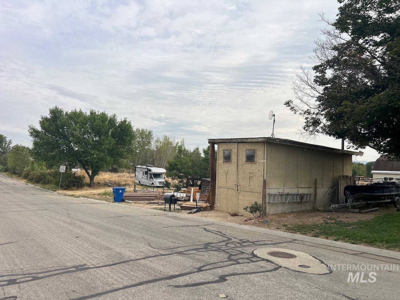 Beige outbuilding beside a paved street, with a boat and RV nearby.