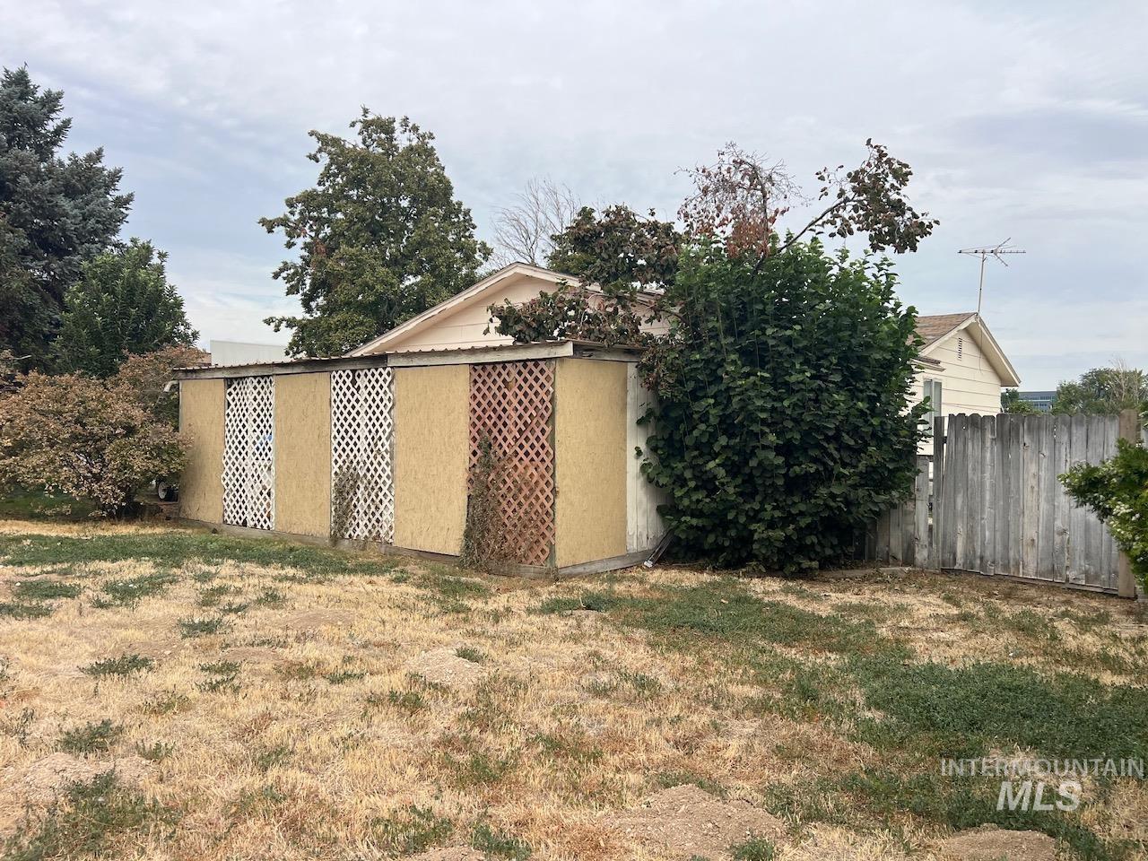 Backyard shed with lattice panels in front of a house, beside a wooden fence and dense shrubs.