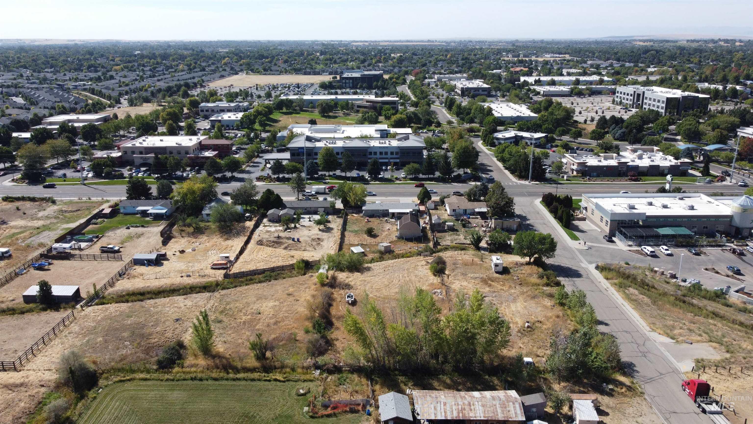 Aerial view of dry vacant land beside a road, with commercial buildings and neighborhoods beyond.