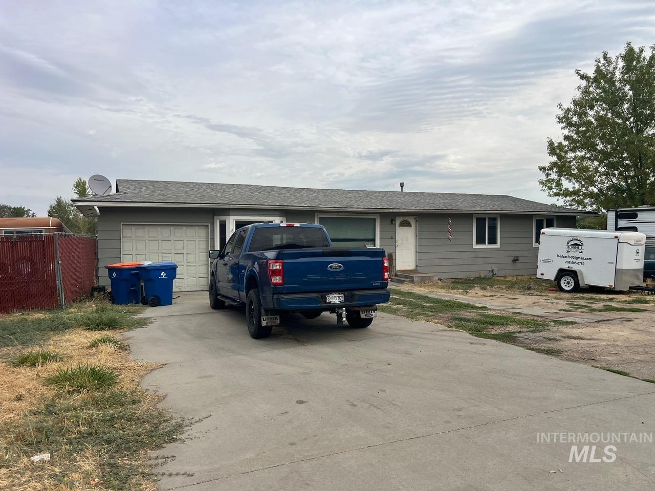 Gray single-story house with an attached garage and a blue pickup parked in the driveway.