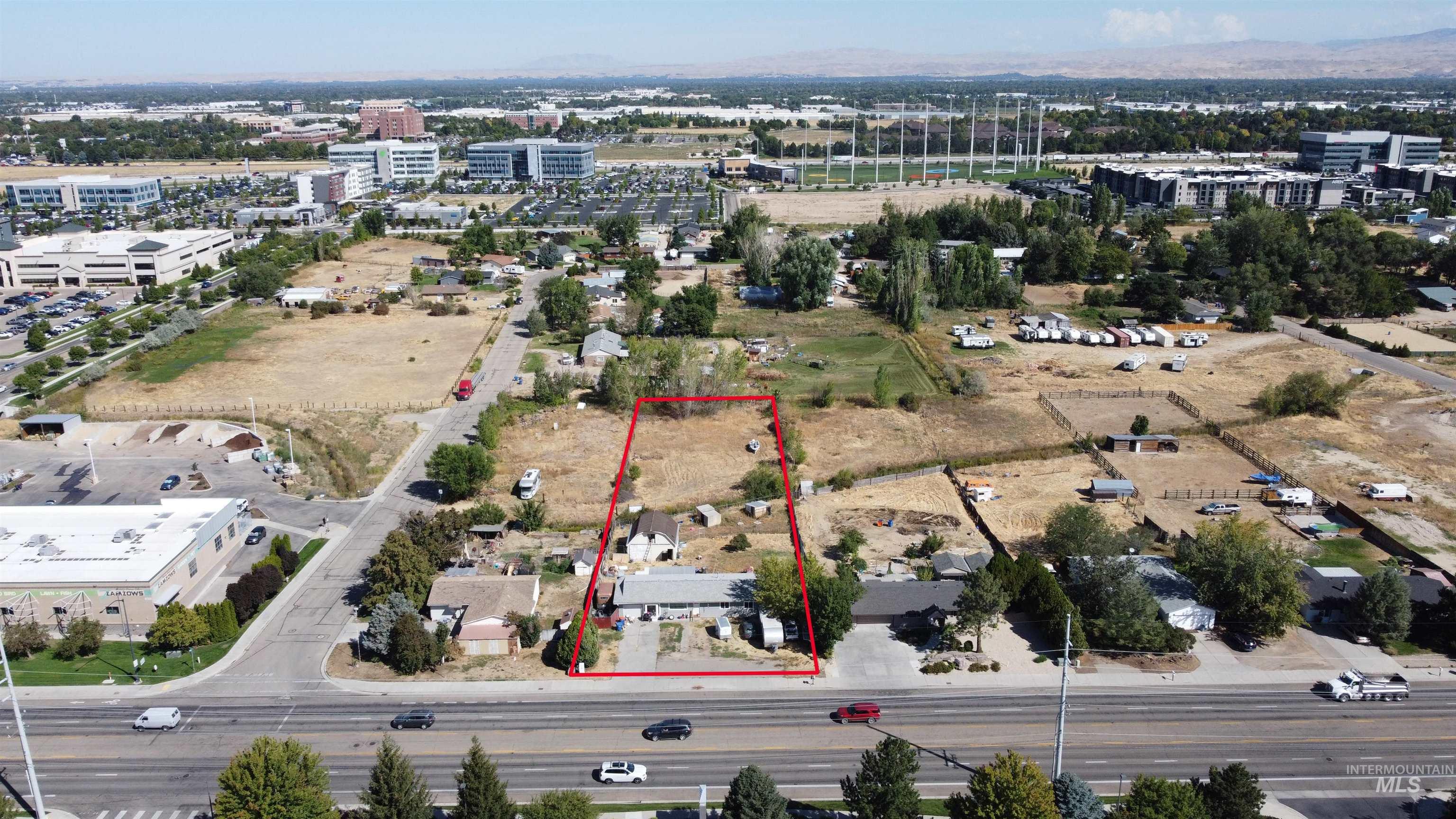 Aerial view of red-outlined property with a house and open land beside a major road.