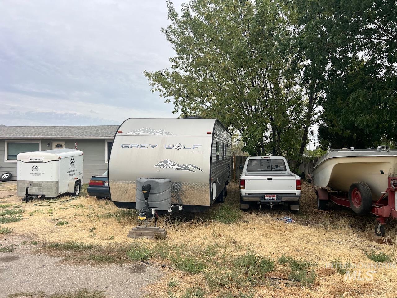 Gray single-story building partly hidden behind parked trailers and a white pickup truck.