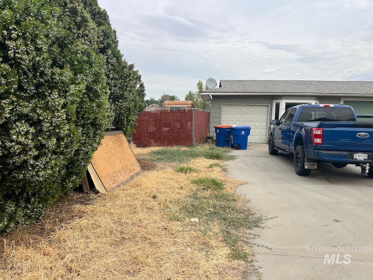 Property garage and driveway beside a dry side yard, flowering hedge, and blue pickup truck.