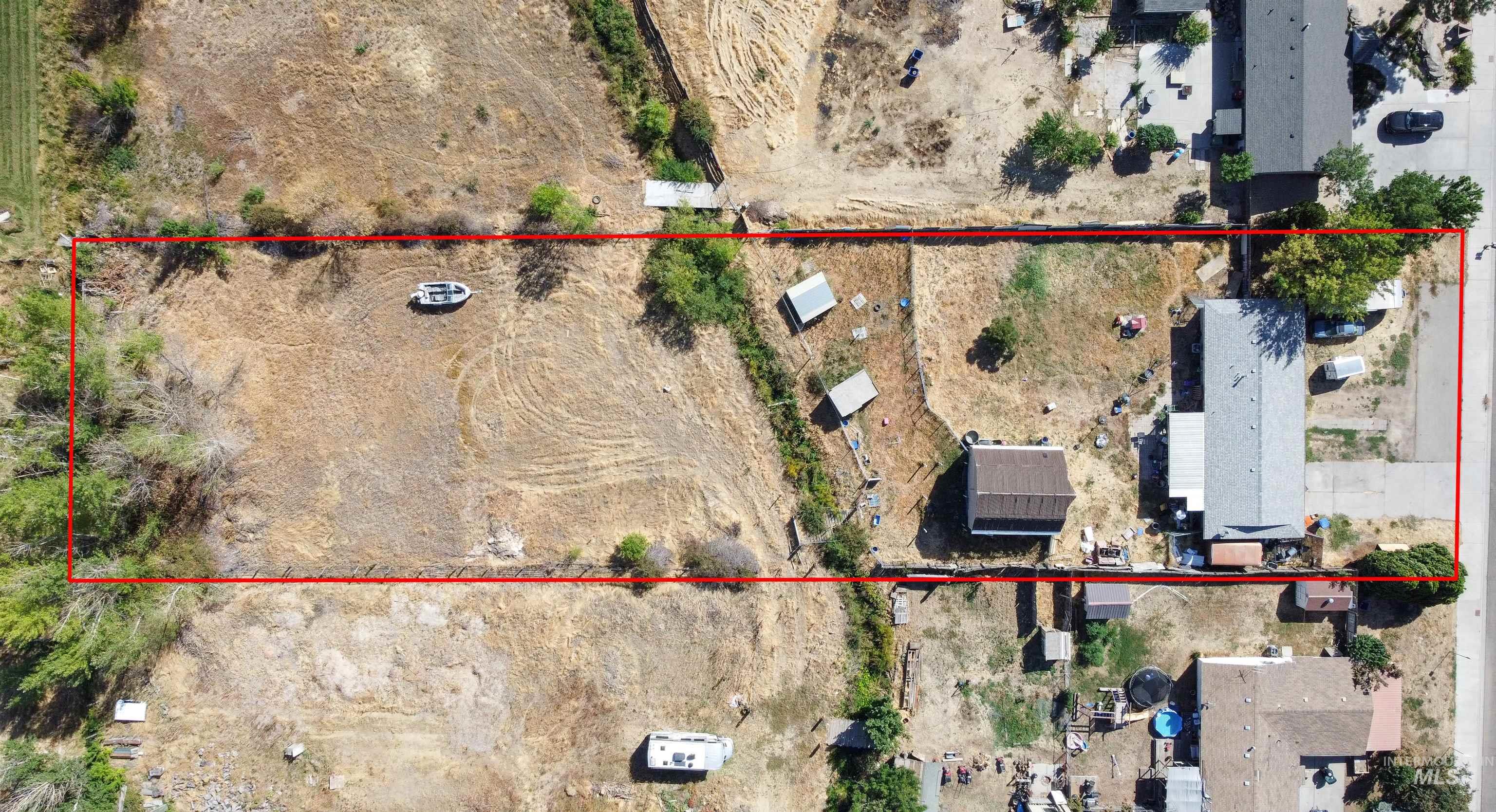 Aerial view of a residential property outlined in red, with a dry open lot beside the house.