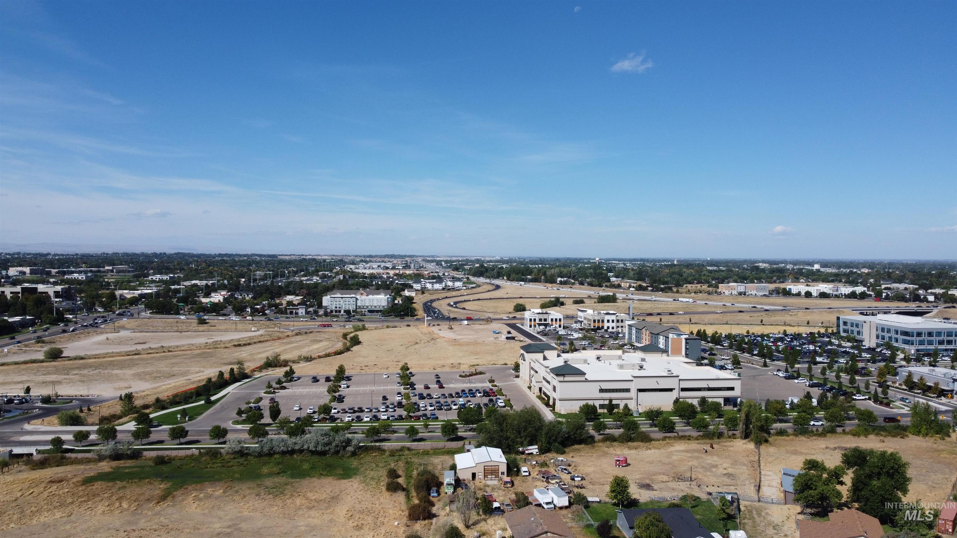 Aerial view of commercial buildings, parking lots, and surrounding open land.