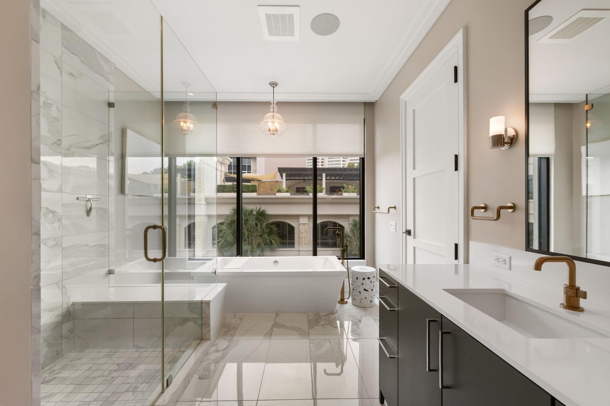 Modern bathroom with a marble shower, freestanding tub, and dark double vanity with brass fixtures.