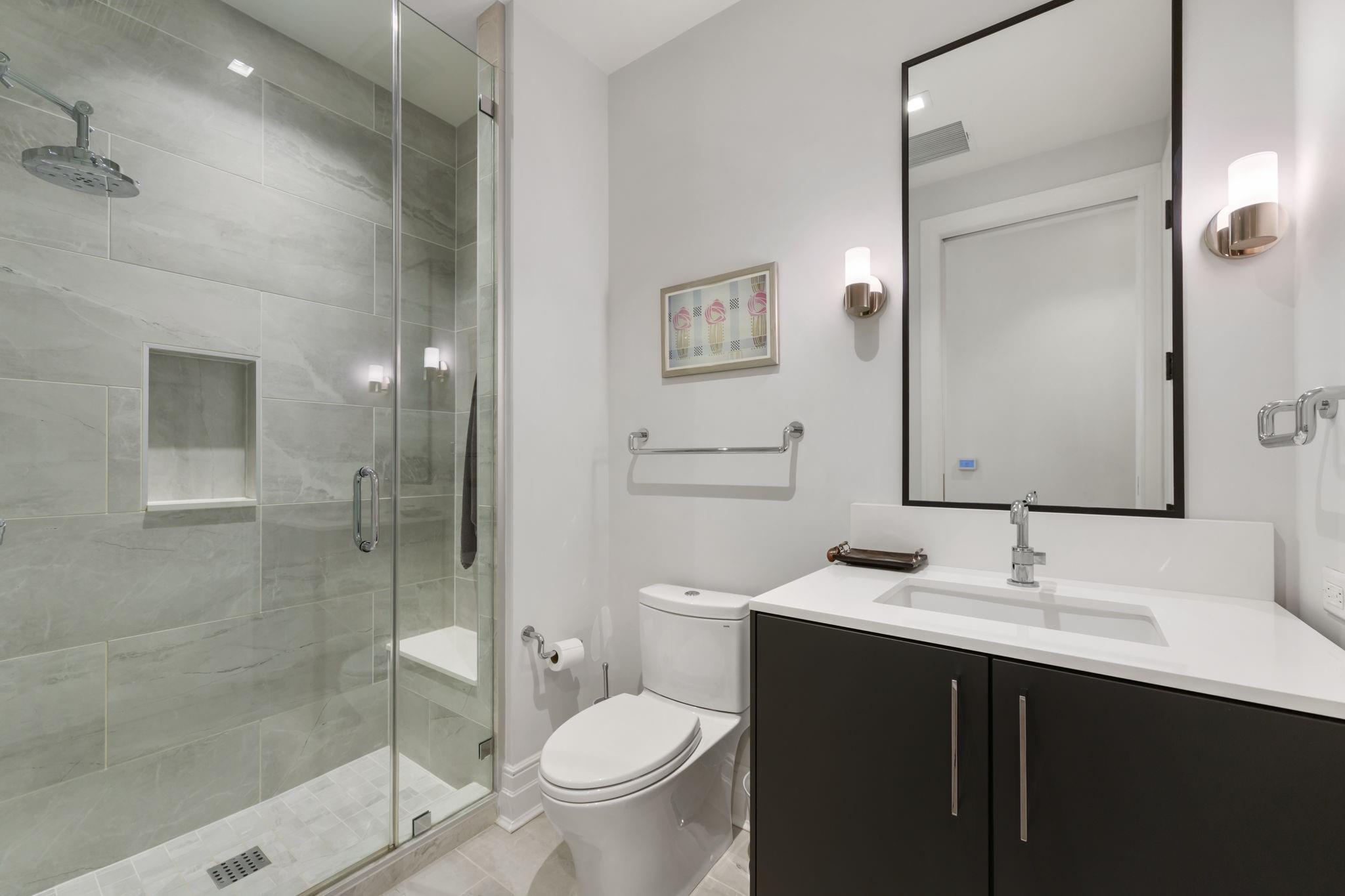 Modern bathroom with a gray-tiled glass shower and dark vanity with a white countertop.