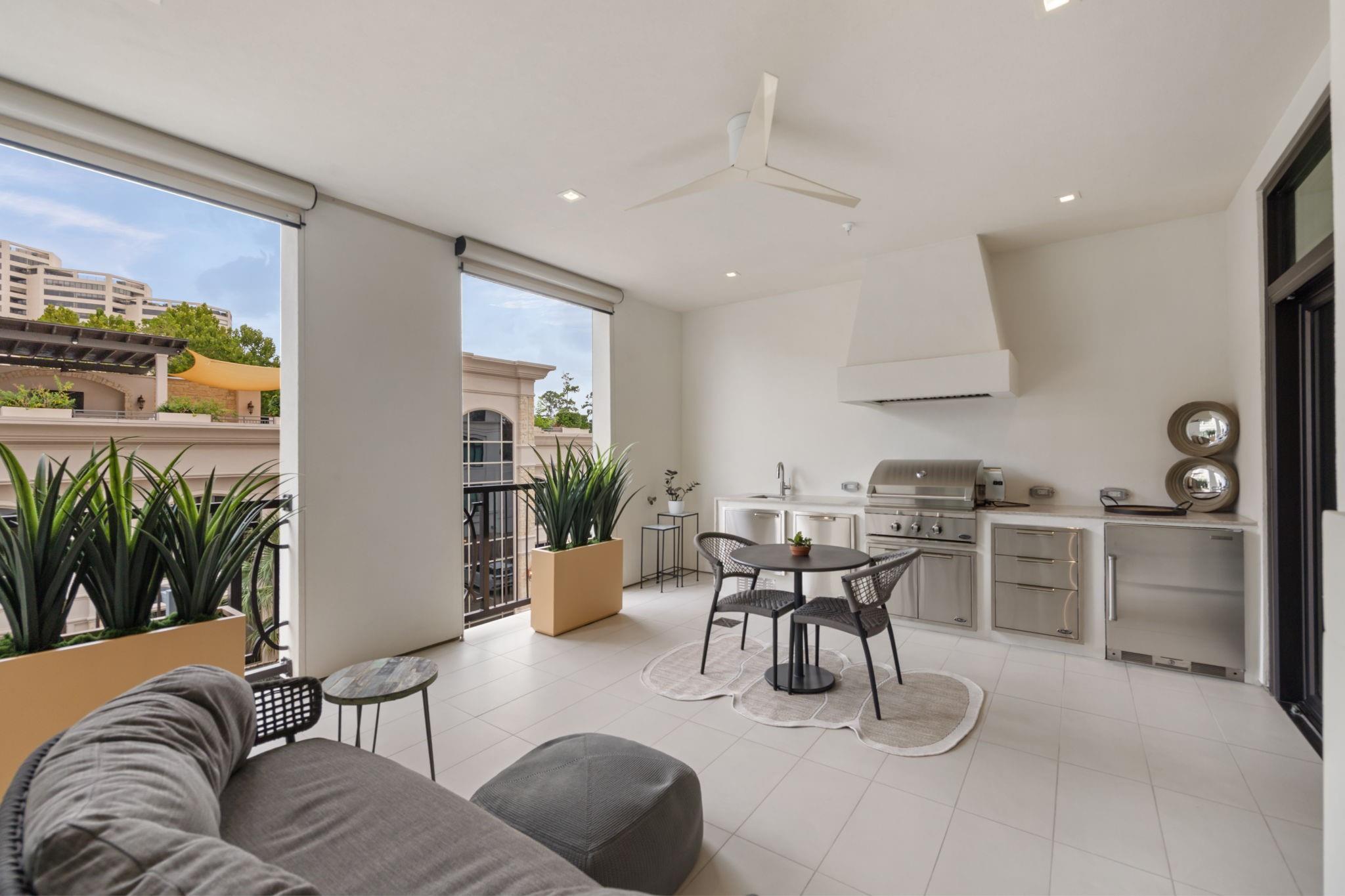 Furnished balcony with a built-in stainless steel grill, round dining set, potted plants, and gray sofa.