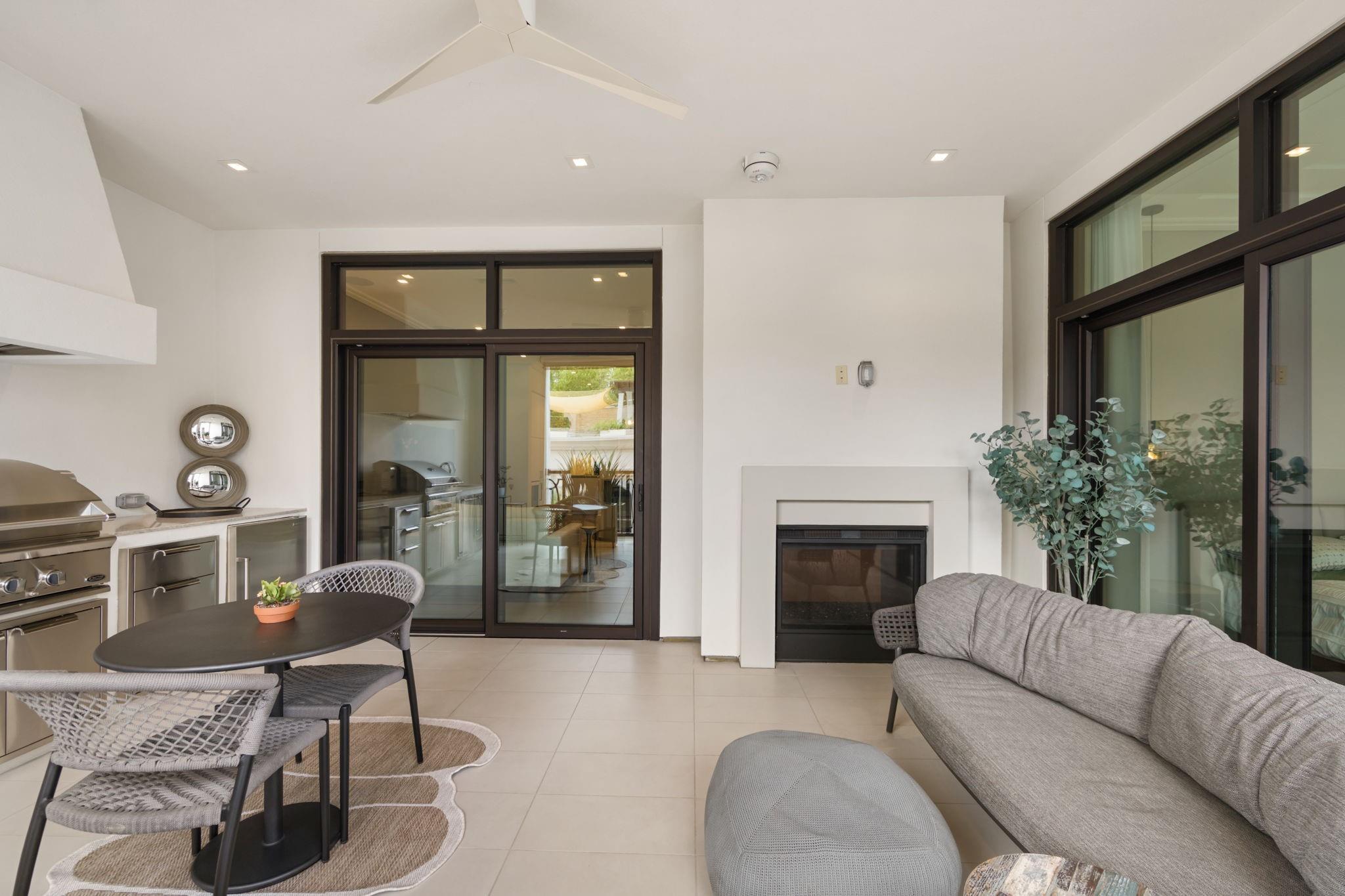 Furnished covered patio with a fireplace, gray sofa, round table, and stainless steel outdoor kitchen.