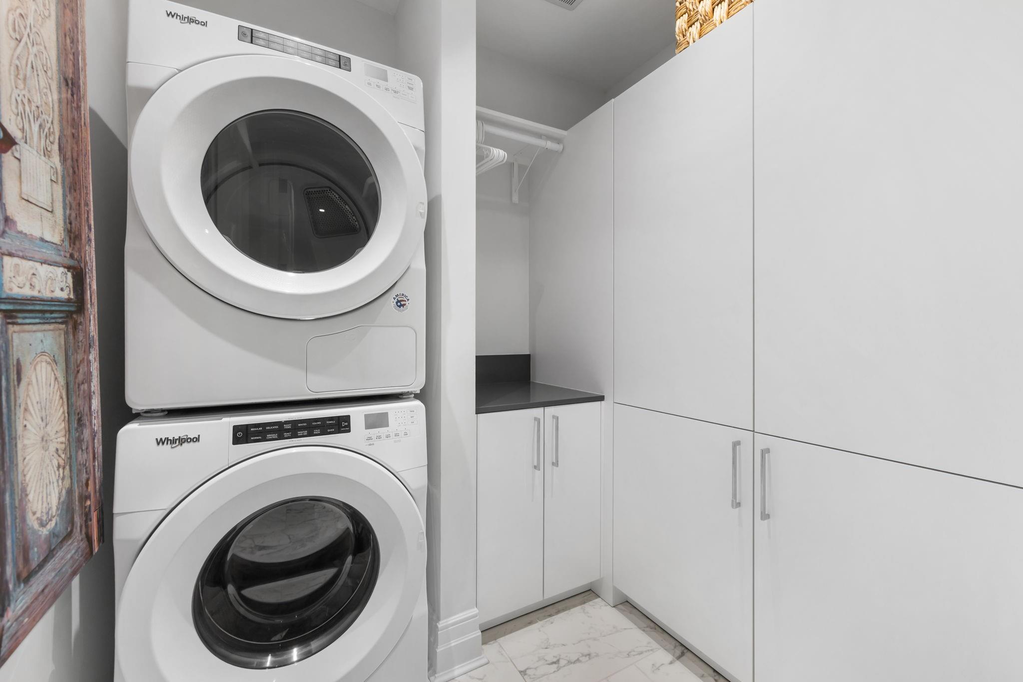 Laundry room with stacked Whirlpool washer and dryer beside built-in white cabinets and a dark countertop.