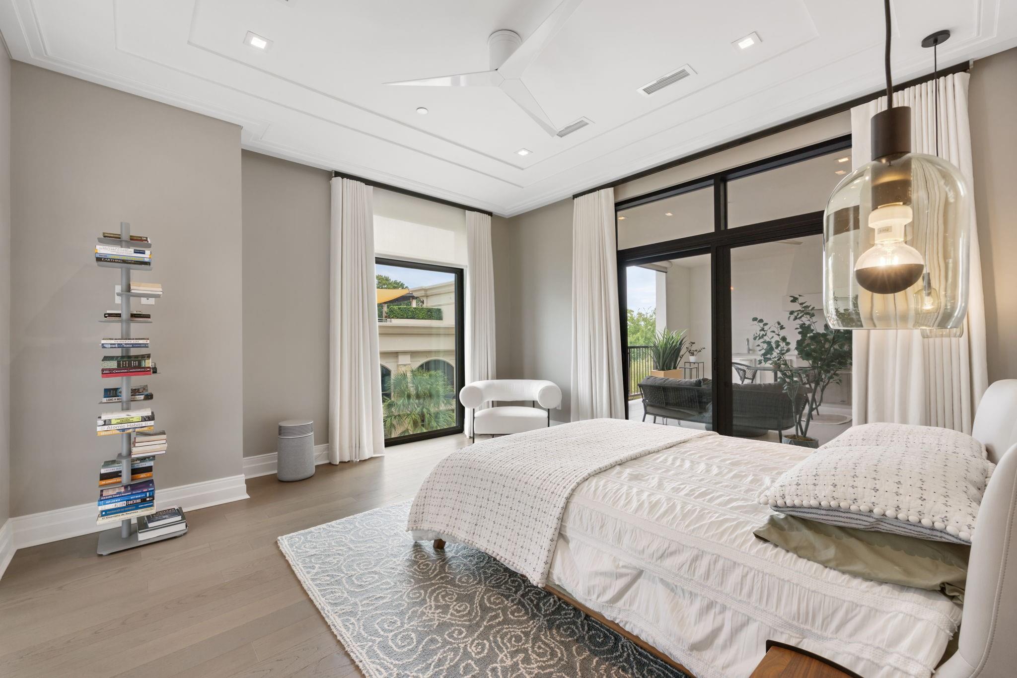 Contemporary bedroom with a white bed, patterned rug, and black-framed glass doors to a balcony.