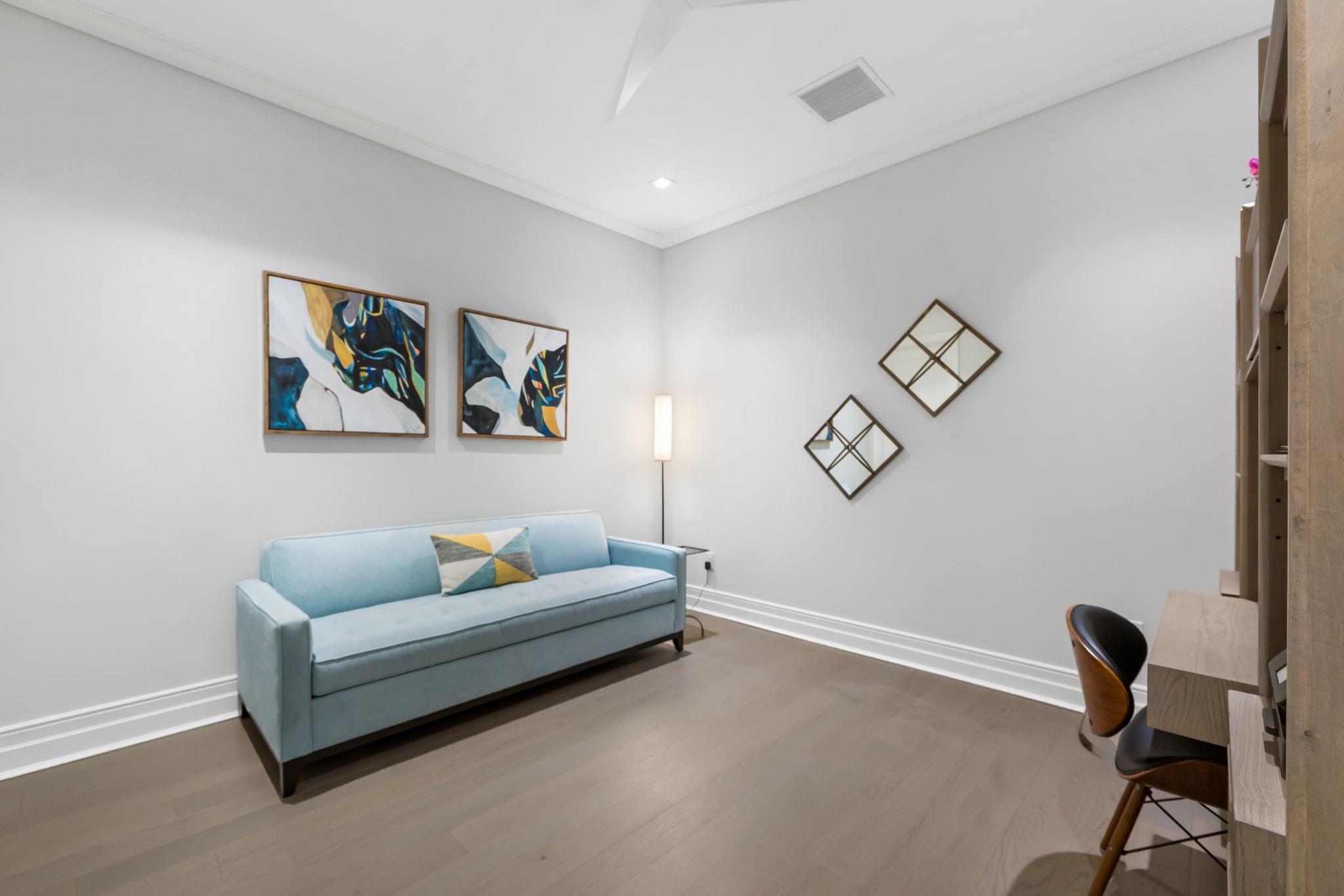 Living room with a light blue sofa, colorful abstract art, geometric mirrors, and built-in desk and shelving.