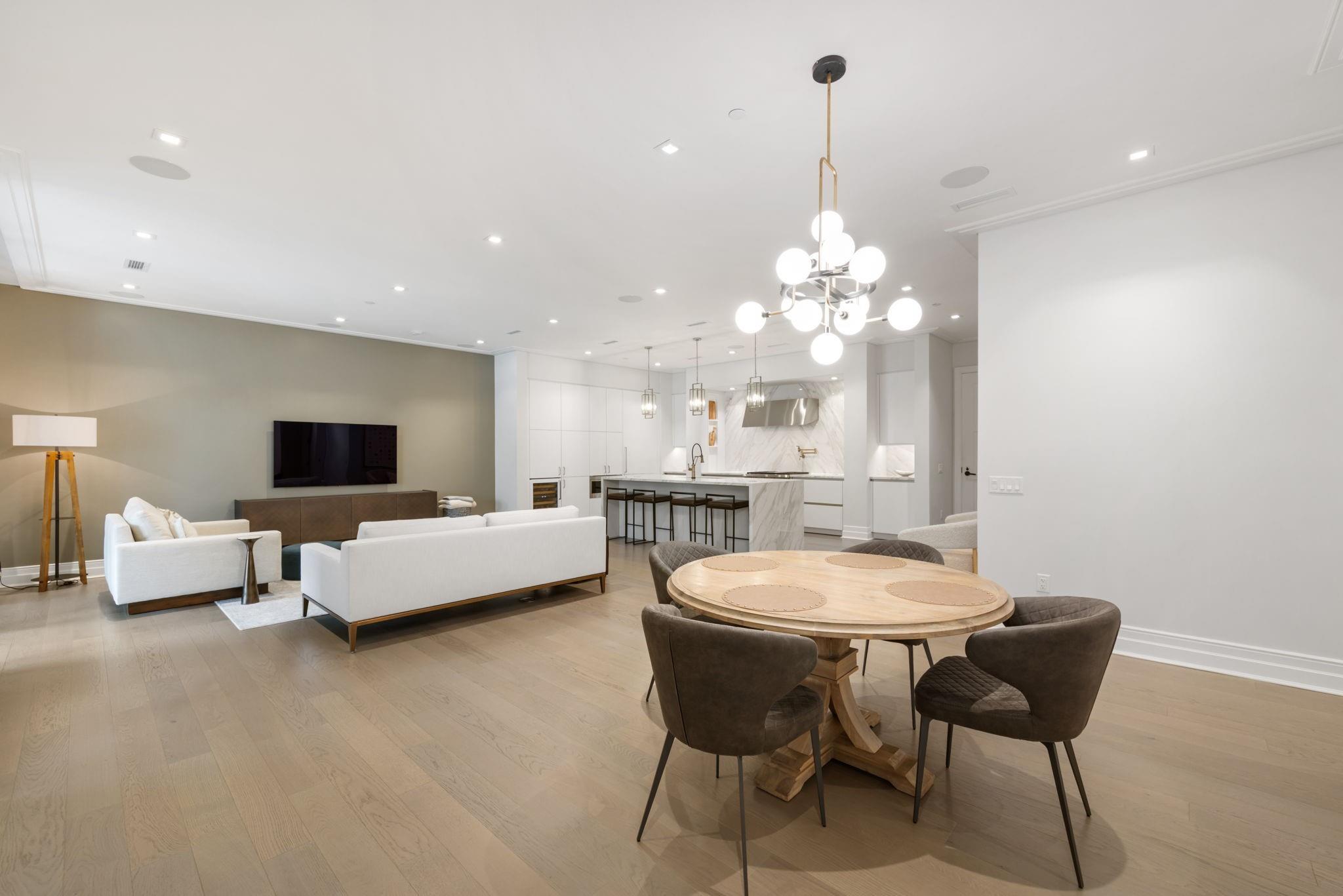 Open-plan condo living room and kitchen with white sofas, marble island, and oval wood dining table.