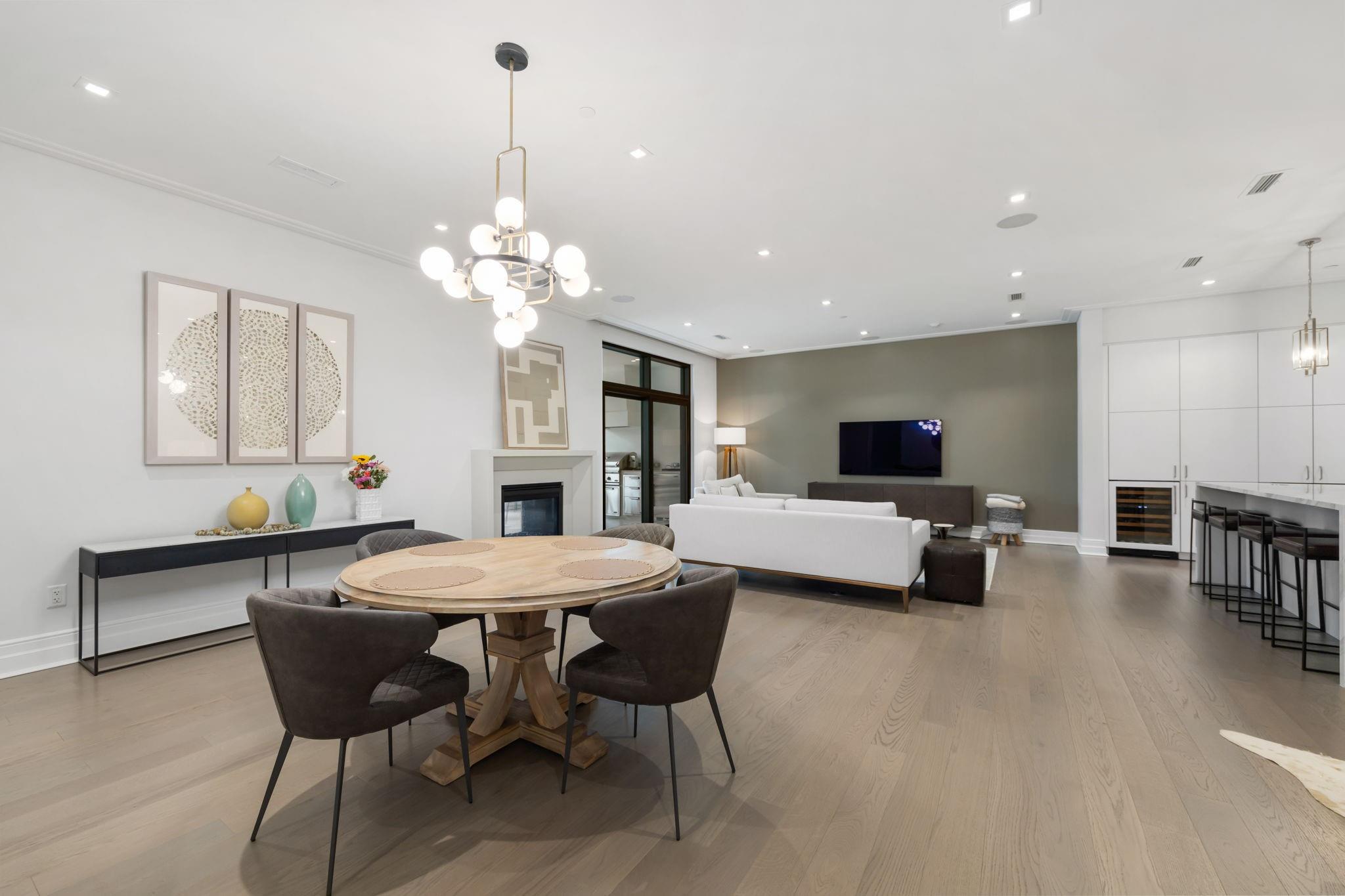 Open-plan living and dining room with a round table, globe chandelier, fireplace, and white kitchen.