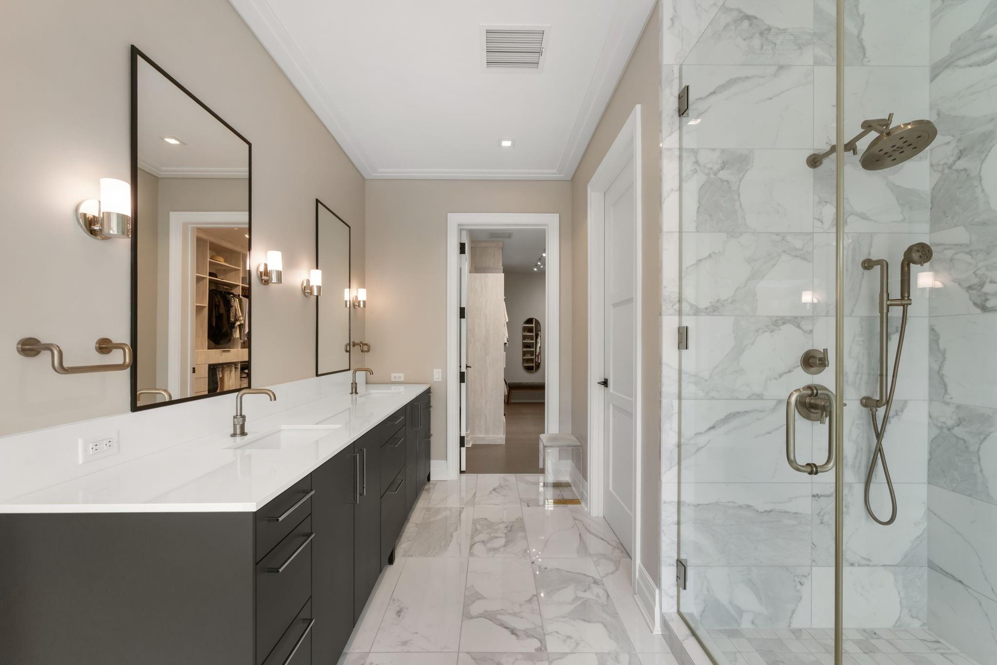 Modern bathroom with a long dark vanity and glass-enclosed marble-look shower.