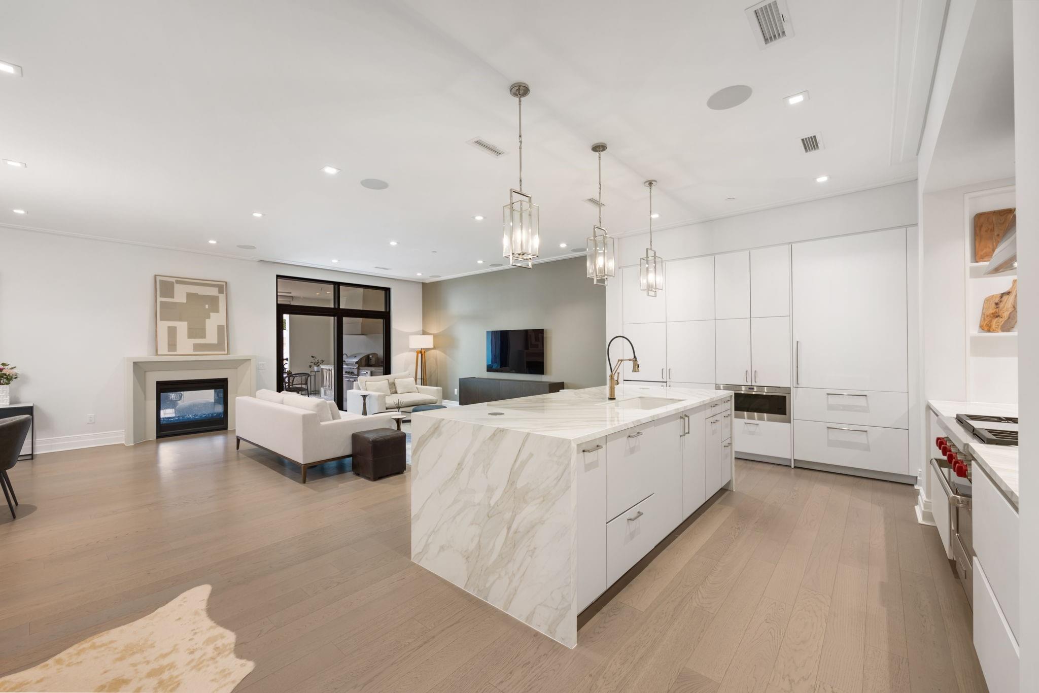 Open-plan kitchen with a marble island, white cabinets, and an adjoining living area.