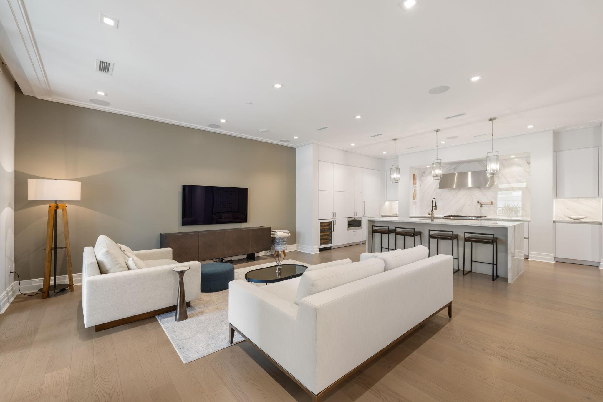 Open-plan living room and kitchen with white sofas, marble backsplash, and a large island.