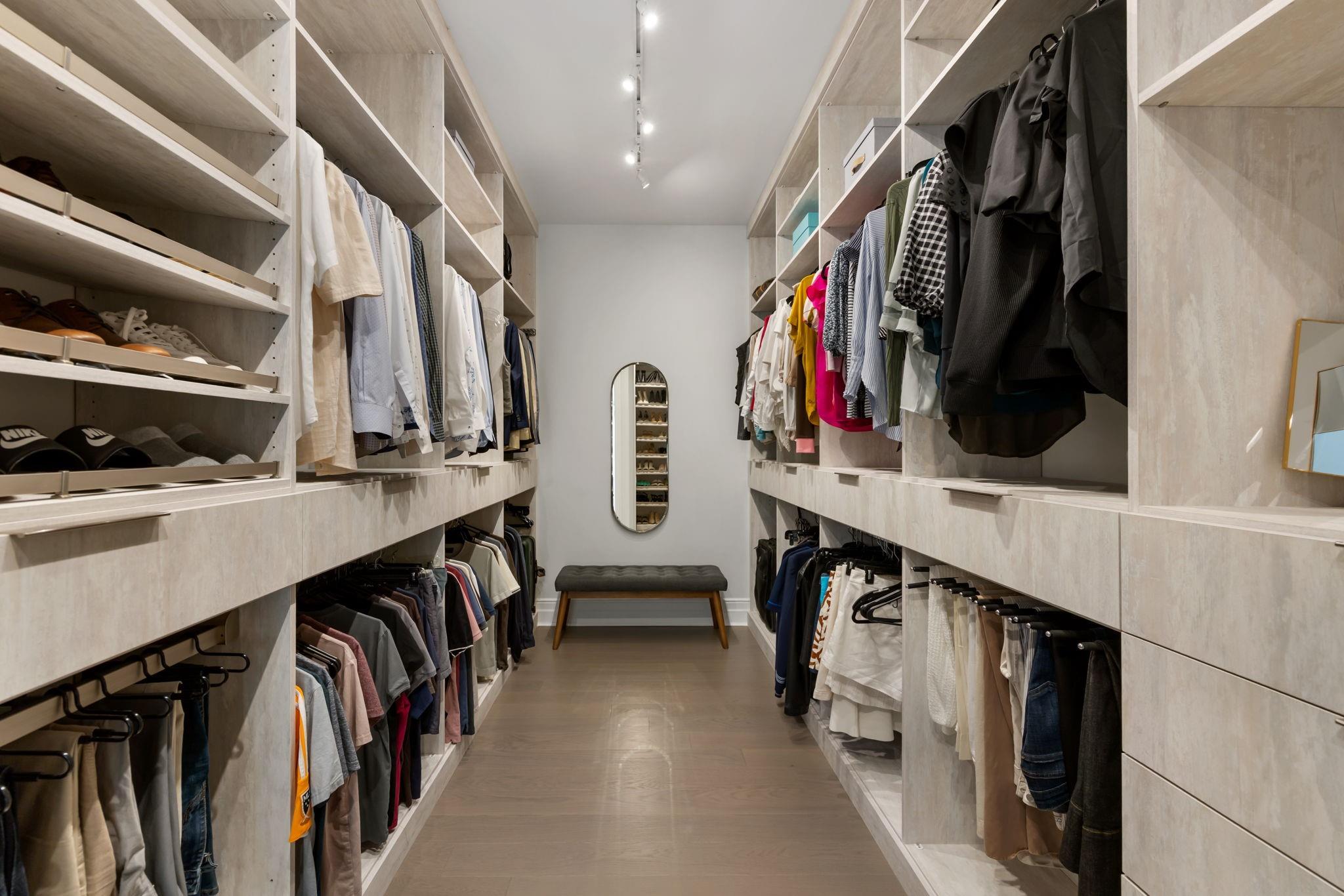 Walk-in closet with built-in shelving, hanging clothes, a bench, and an oval mirror.
