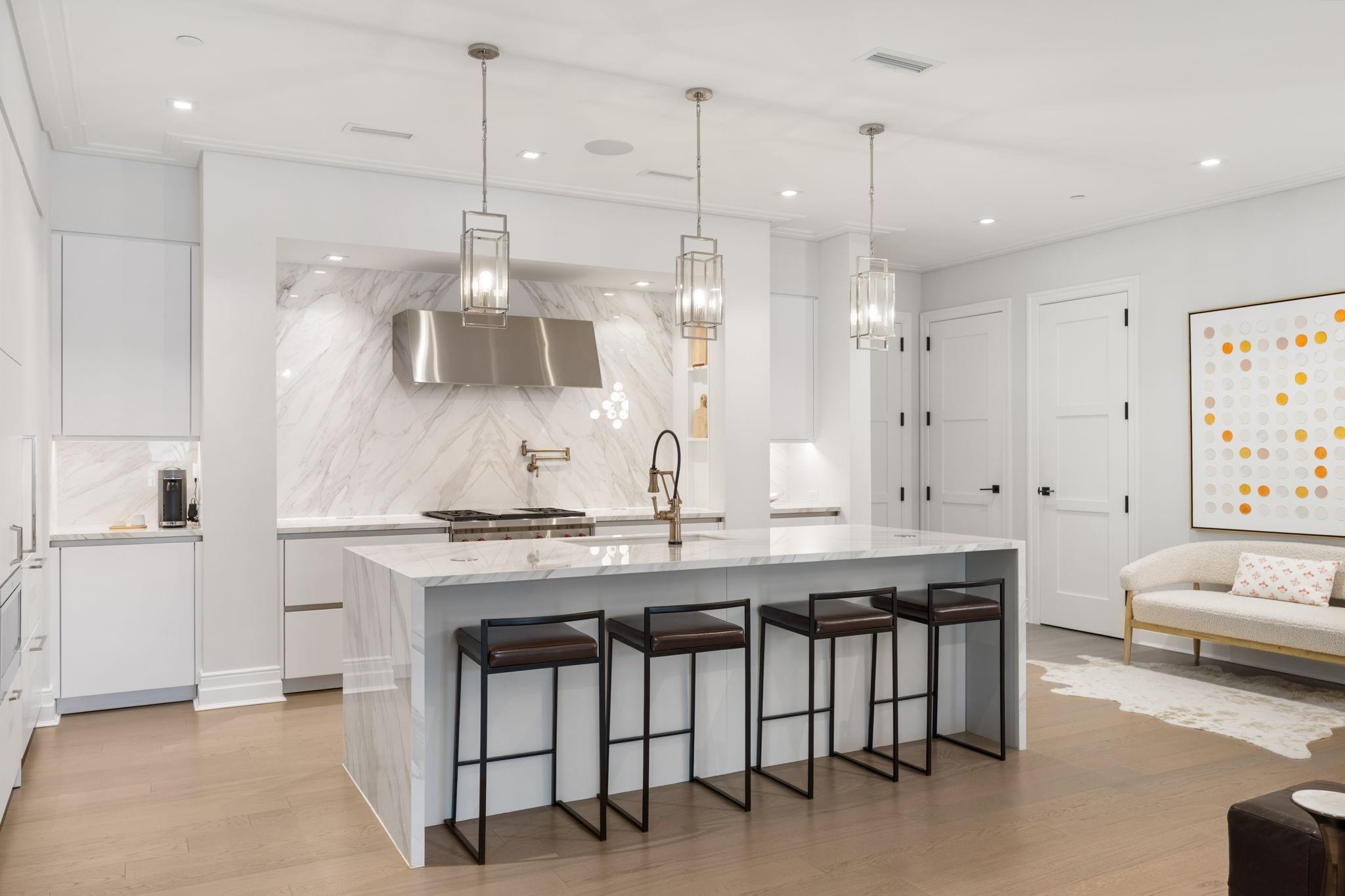 Modern kitchen with marble island, four bar stools, veined backsplash, and pendant lights.