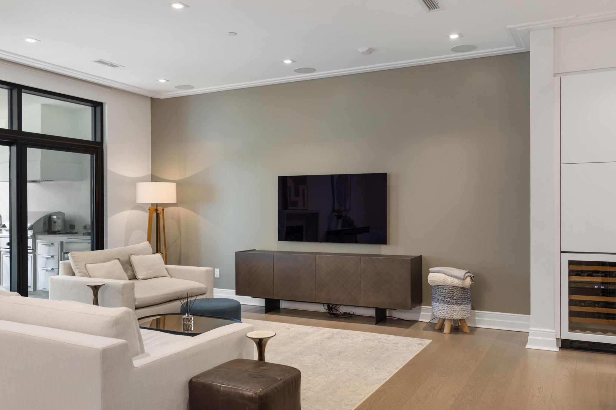 Living room with cream sofas, a wall-mounted television, black-framed glass doors, and a built-in wine refrigerator.