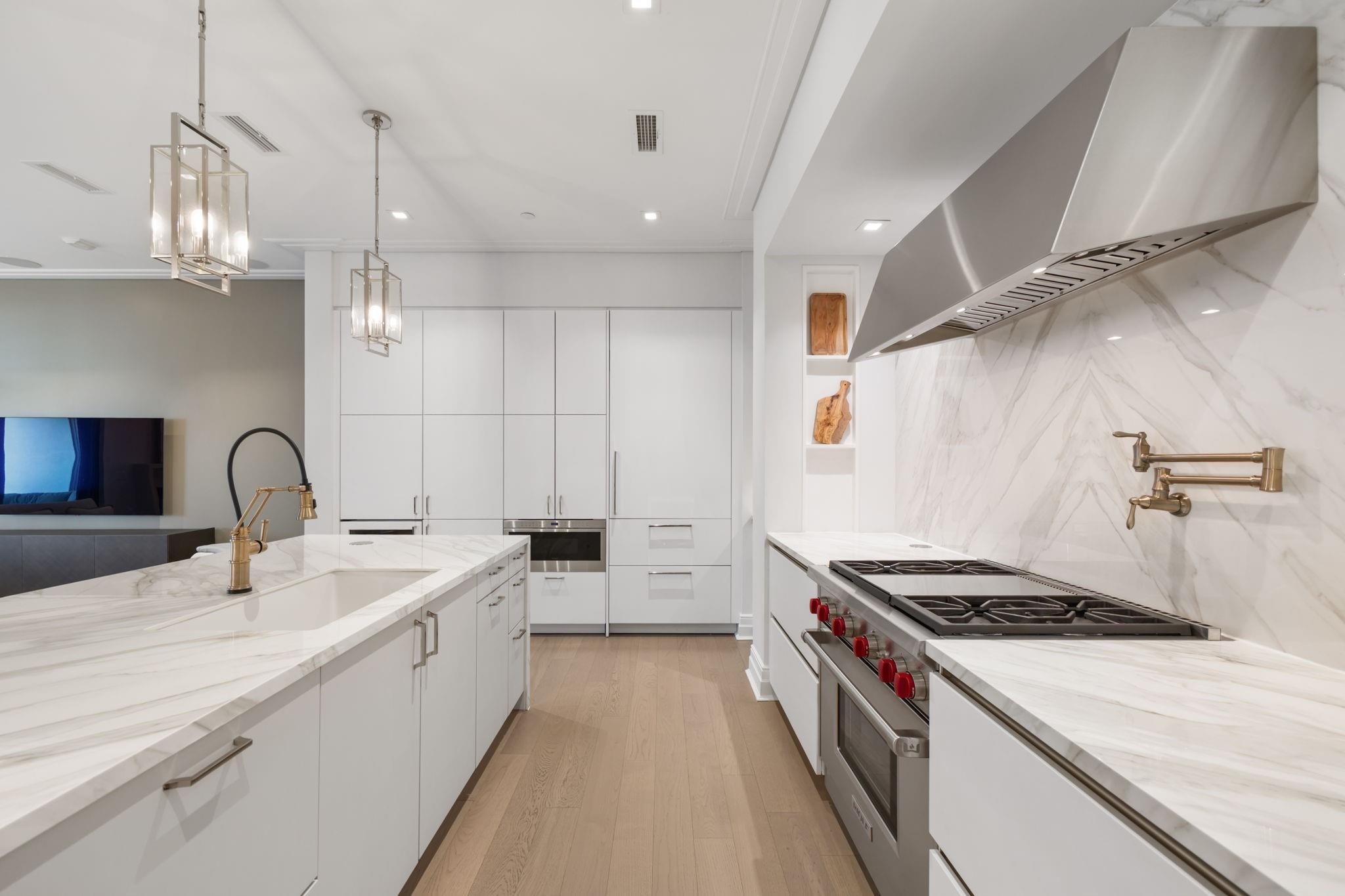 Modern white kitchen with marble island, brass fixtures, and a stainless-steel gas range.