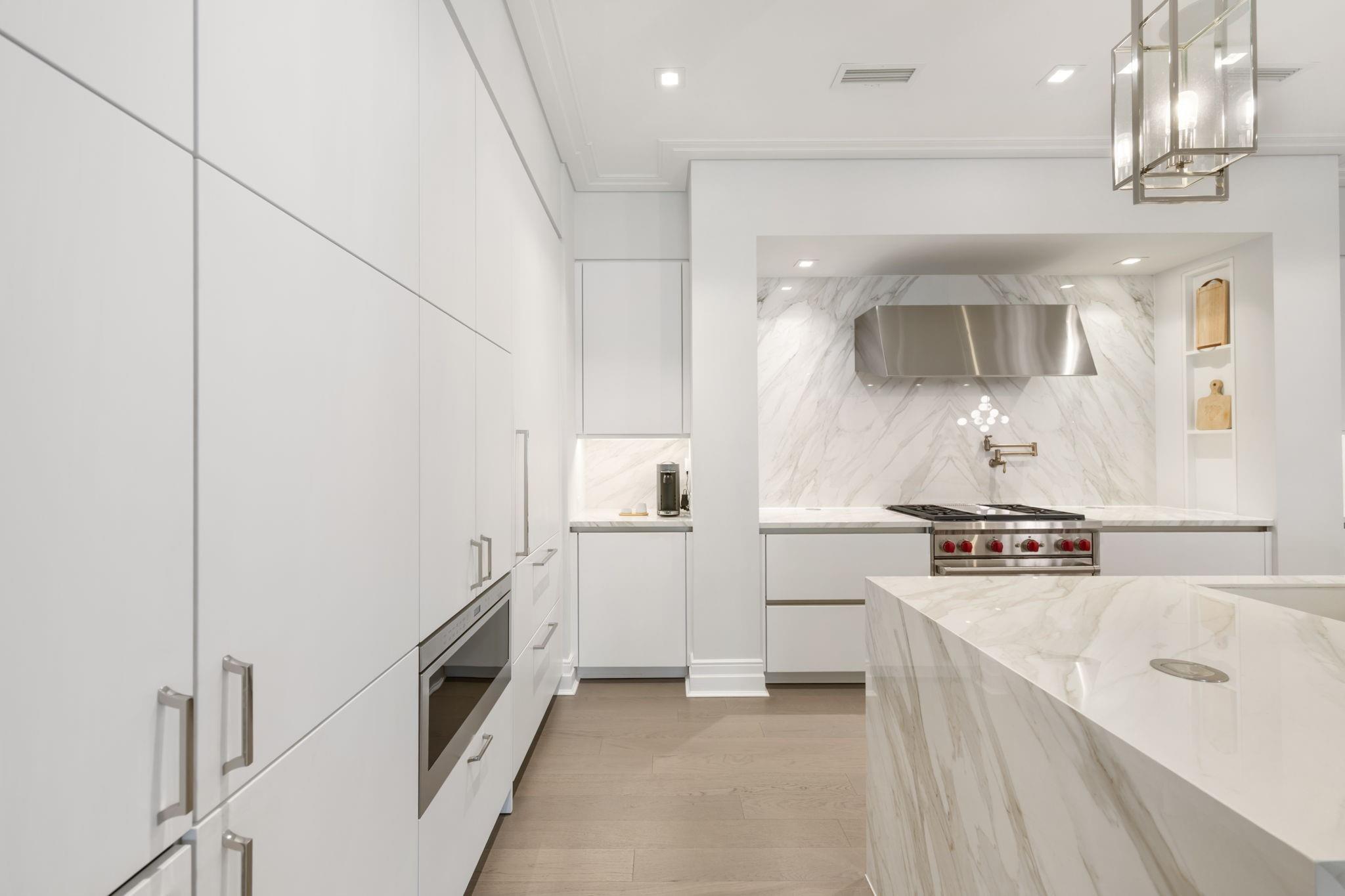 Modern white kitchen with a marble waterfall island, stainless steel range, and brass fixtures.