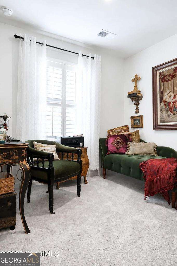 Furnished sitting room with green seating, patterned cushions, and tall windows with plantation shutters.