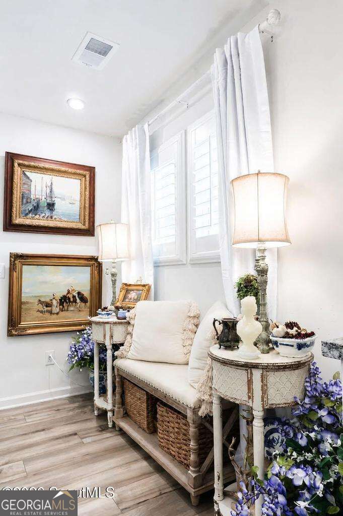 Sitting nook with a white cushioned bench, ornate tables, framed artwork, and shuttered windows.