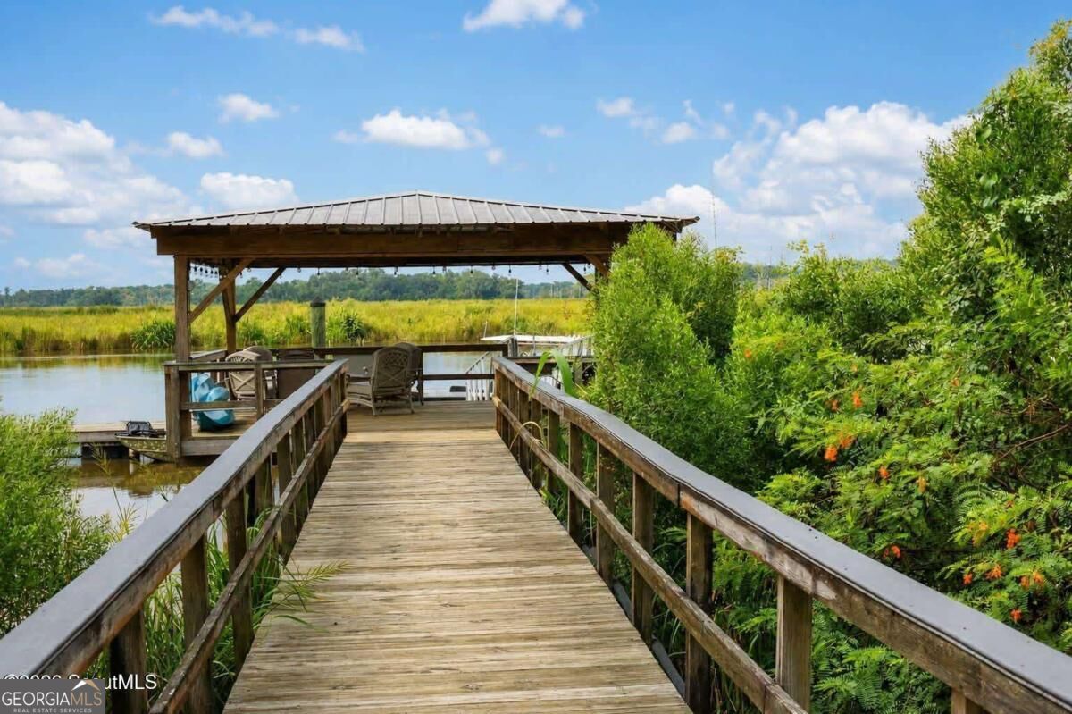 Wooden boardwalk leads to a covered seating dock overlooking marsh water.