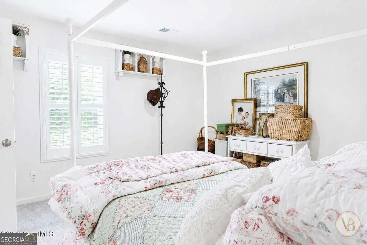 Bedroom with a white four-poster bed, floral quilts, plantation shutters, and wicker baskets.