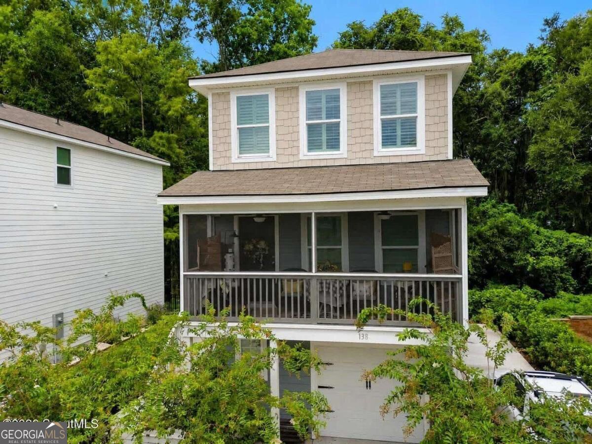 Two-story house with a covered, furnished porch and garage below, surrounded by trees.