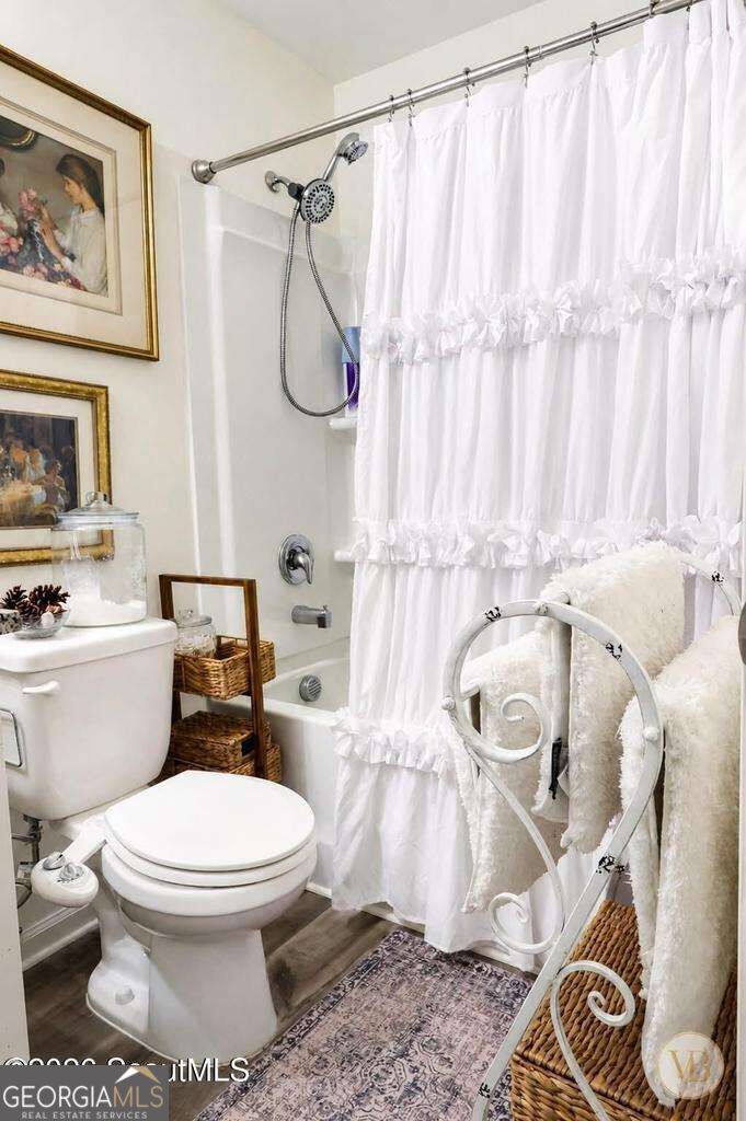 Bathroom with a white ruffled shower curtain, toilet, framed art, and decorative chair holding towels.
