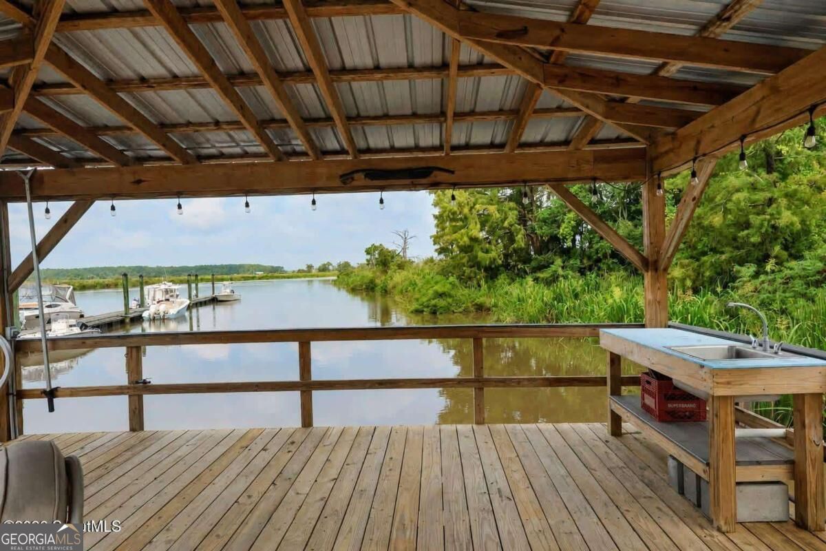 Covered wooden dock overlooking a waterway, with moored boats and an outdoor sink.