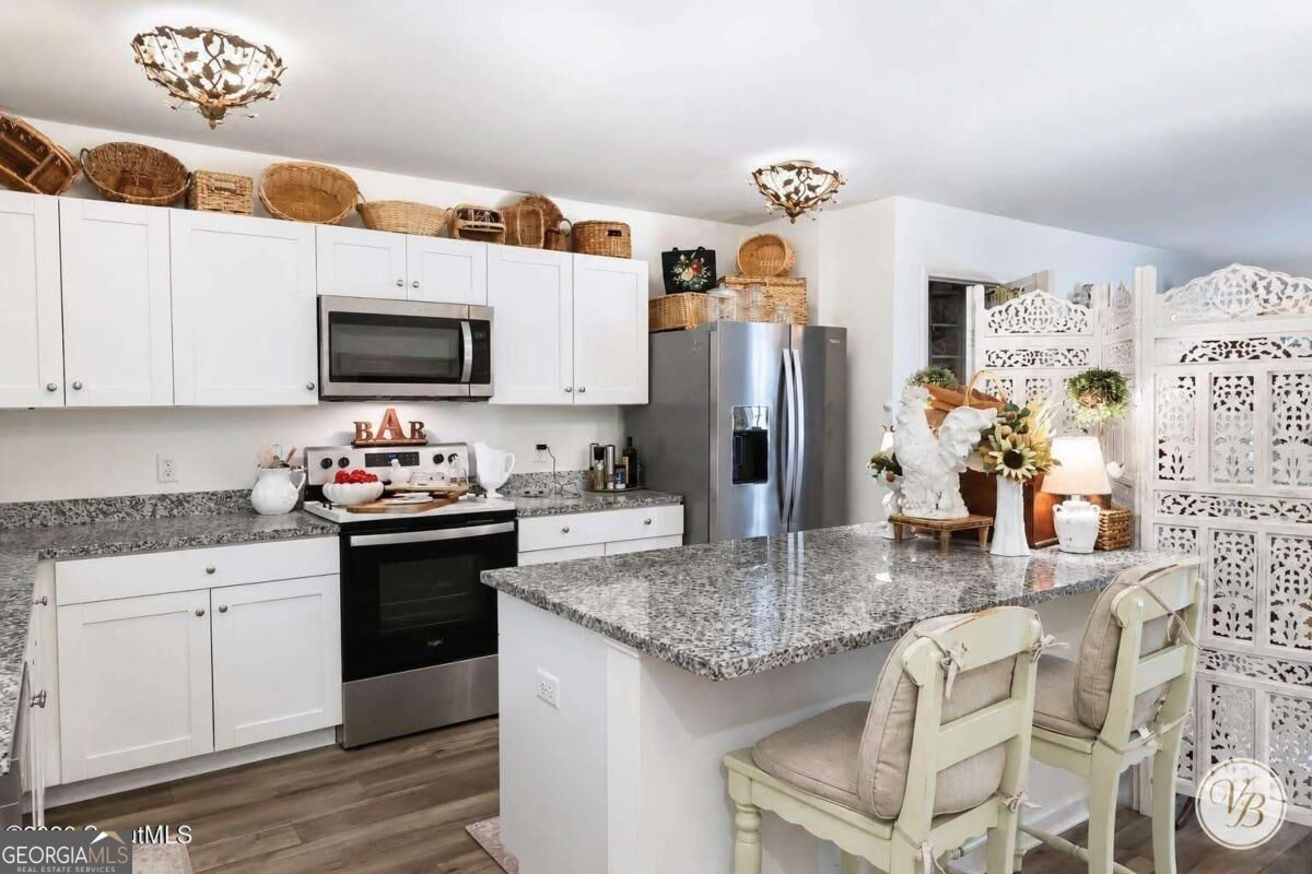 Kitchen with a granite island, white cabinetry, stainless-steel appliances, and a carved folding screen.