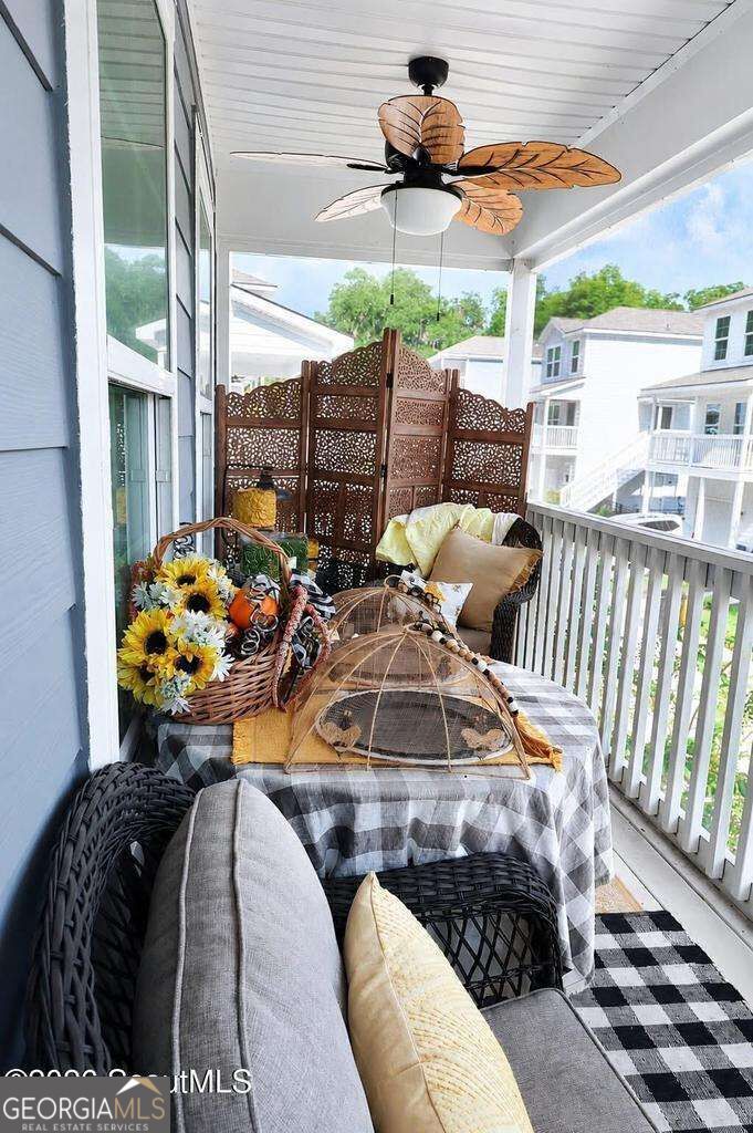 Covered porch with wicker seating, a checkered table, decorative screen, and leaf-blade ceiling fan.