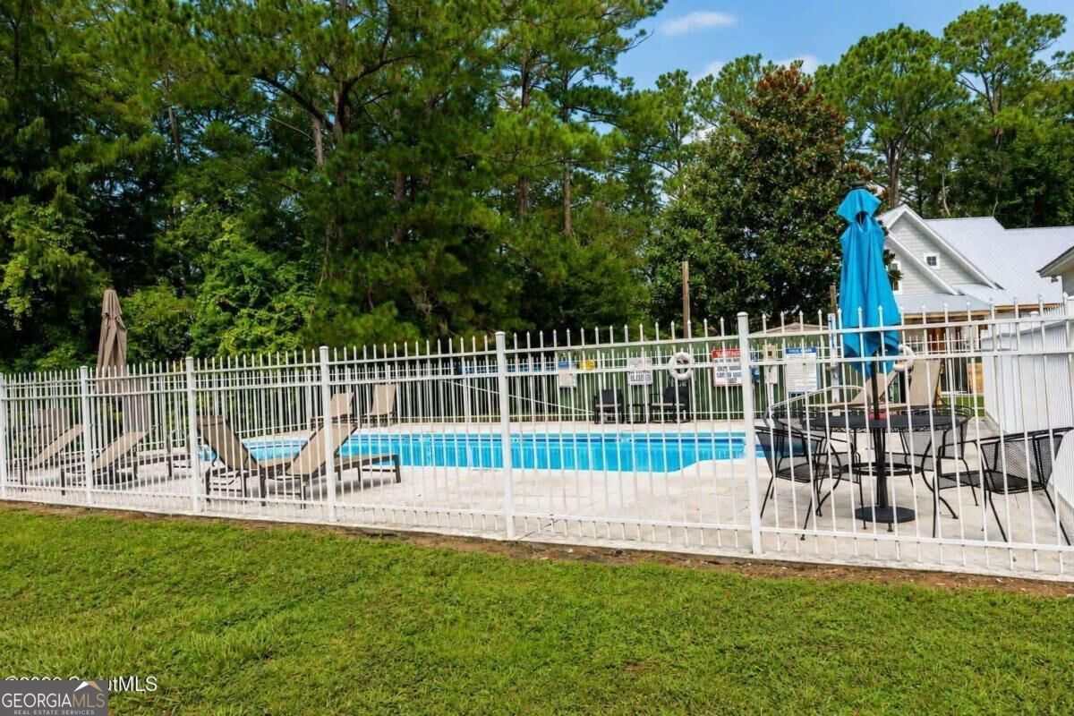 Fenced outdoor pool with lounge chairs, patio dining set, and closed umbrellas.