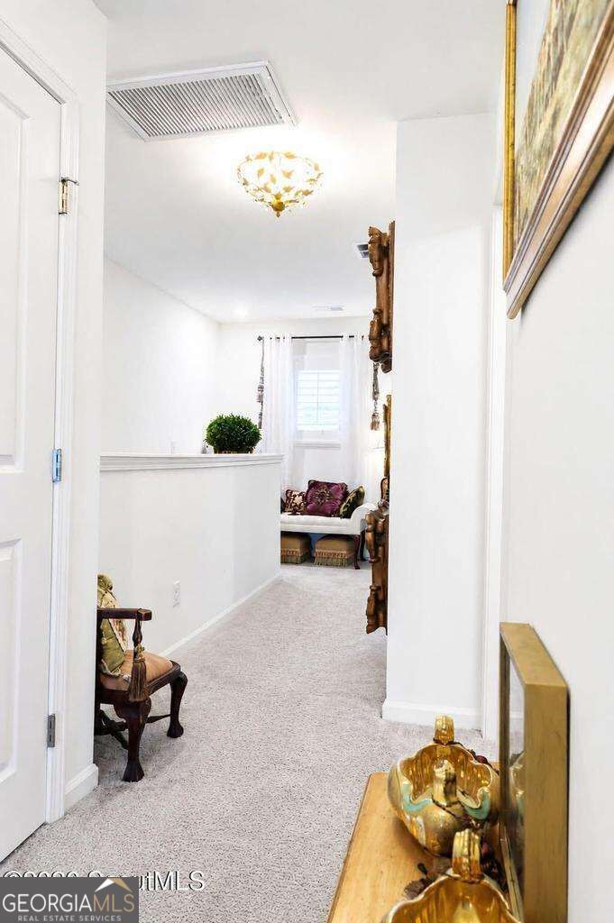 Carpeted hallway with a white divider, chandelier, decorative furnishings, and a sitting area at the end.