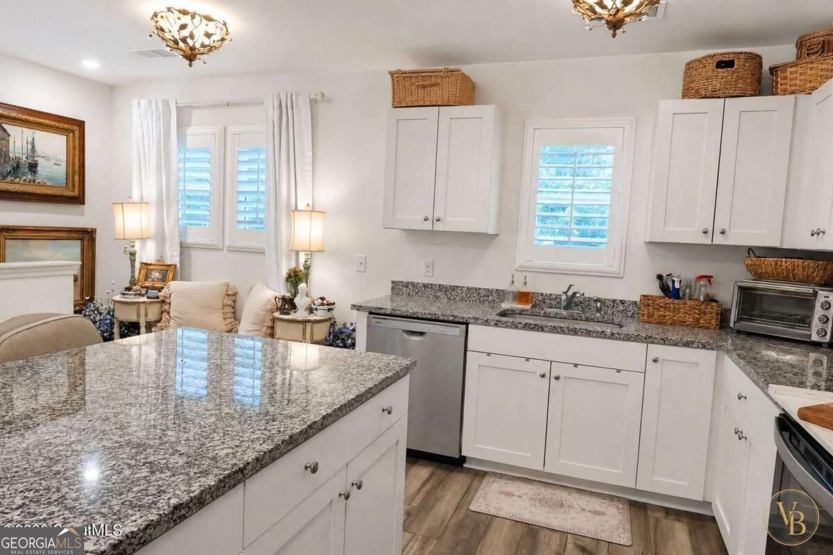 Kitchen with white cabinetry, granite counters, a large peninsula, and a sitting area by shuttered windows.