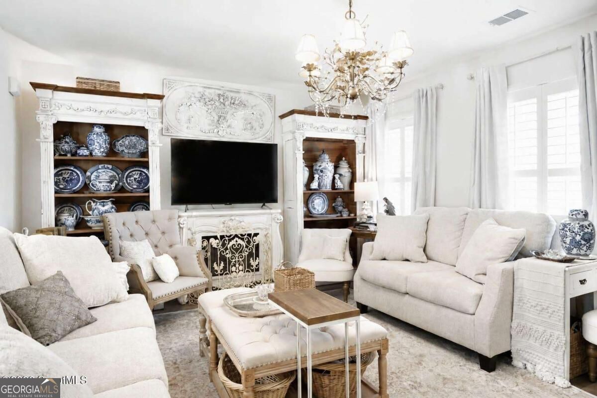 Living room with white sofas, ornate fireplace, blue-and-white ceramics, and chandelier.