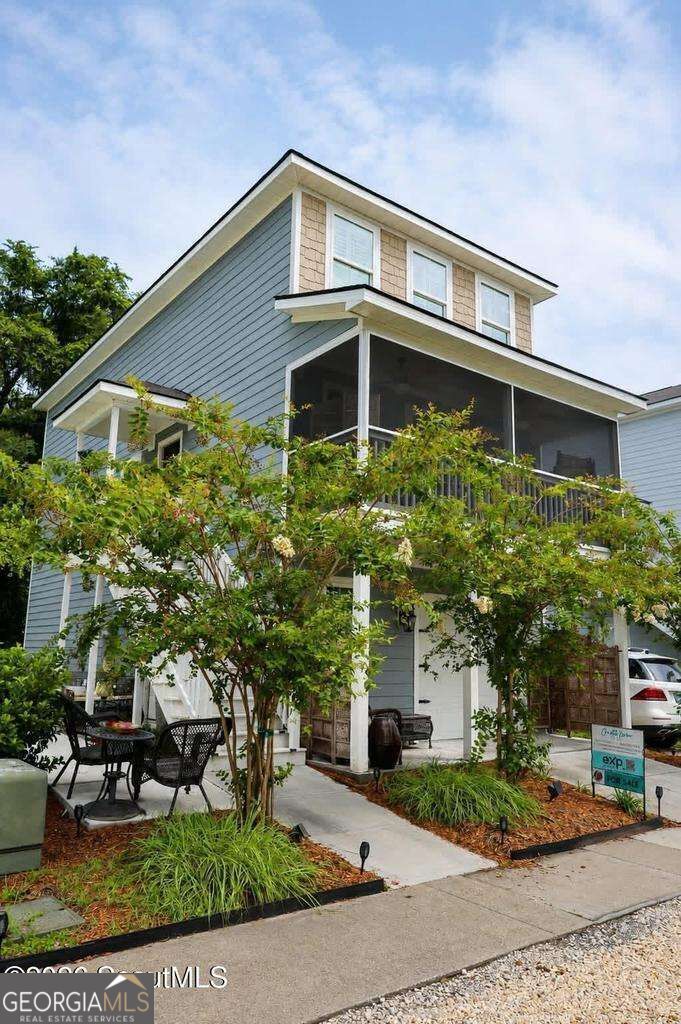 Blue two-story house with a covered porch, patio seating, and leafy landscaping.
