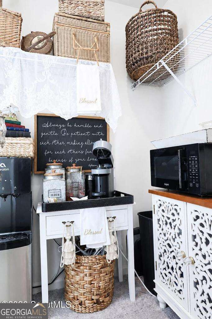 Kitchen coffee station with a microwave, coffee maker, woven baskets, and white storage cabinets.