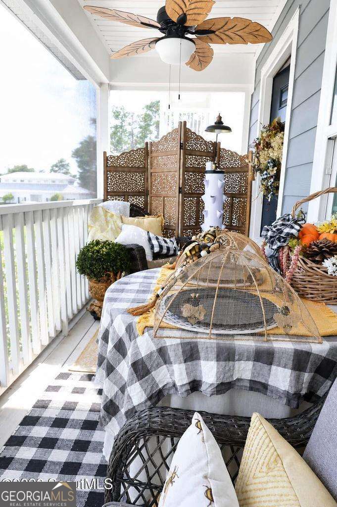 Covered porch with wicker seating, a checkered table, autumn decorations, and a leaf-shaped ceiling fan.