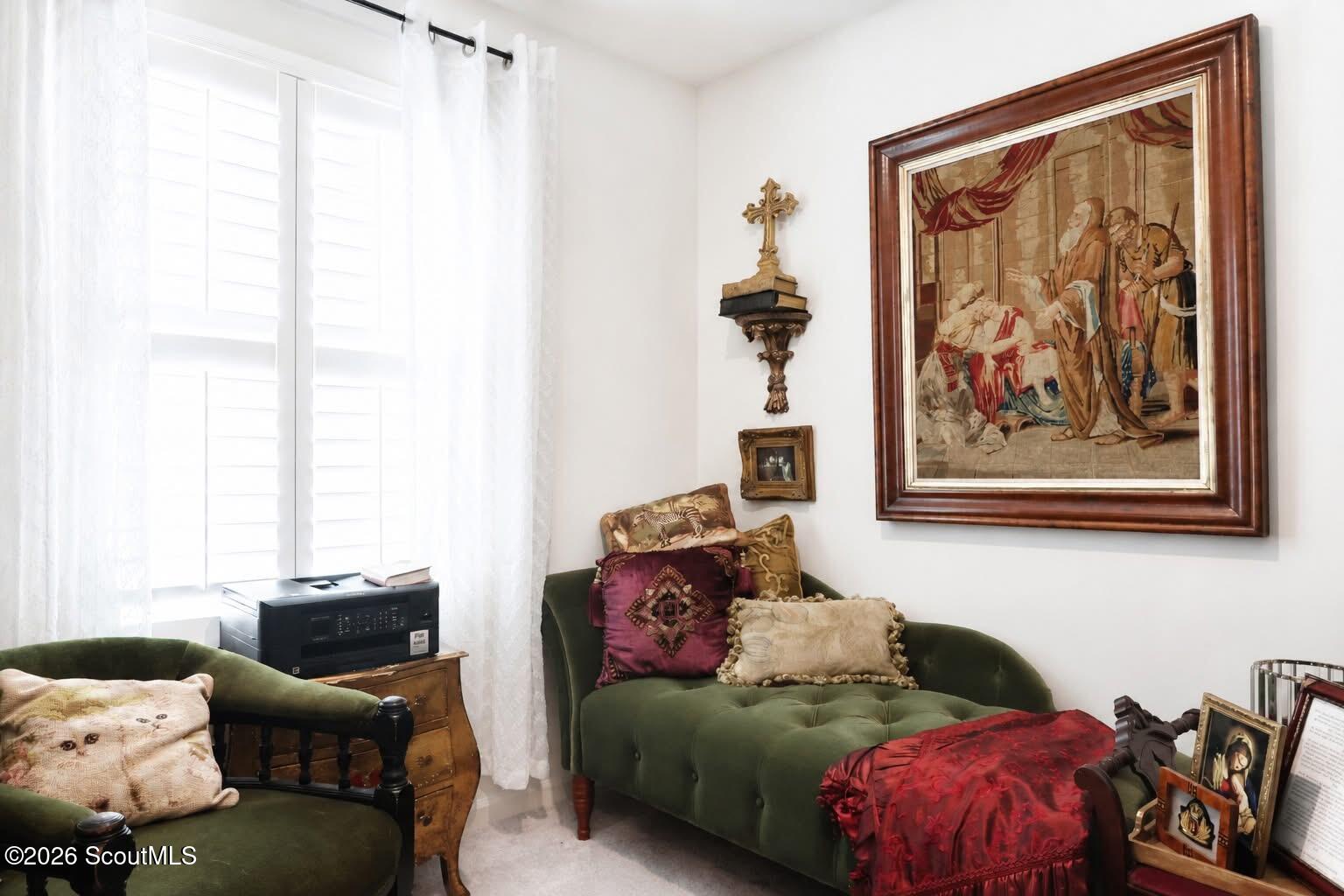 Furnished sitting room with green seating, a shuttered window, and large framed religious artwork.