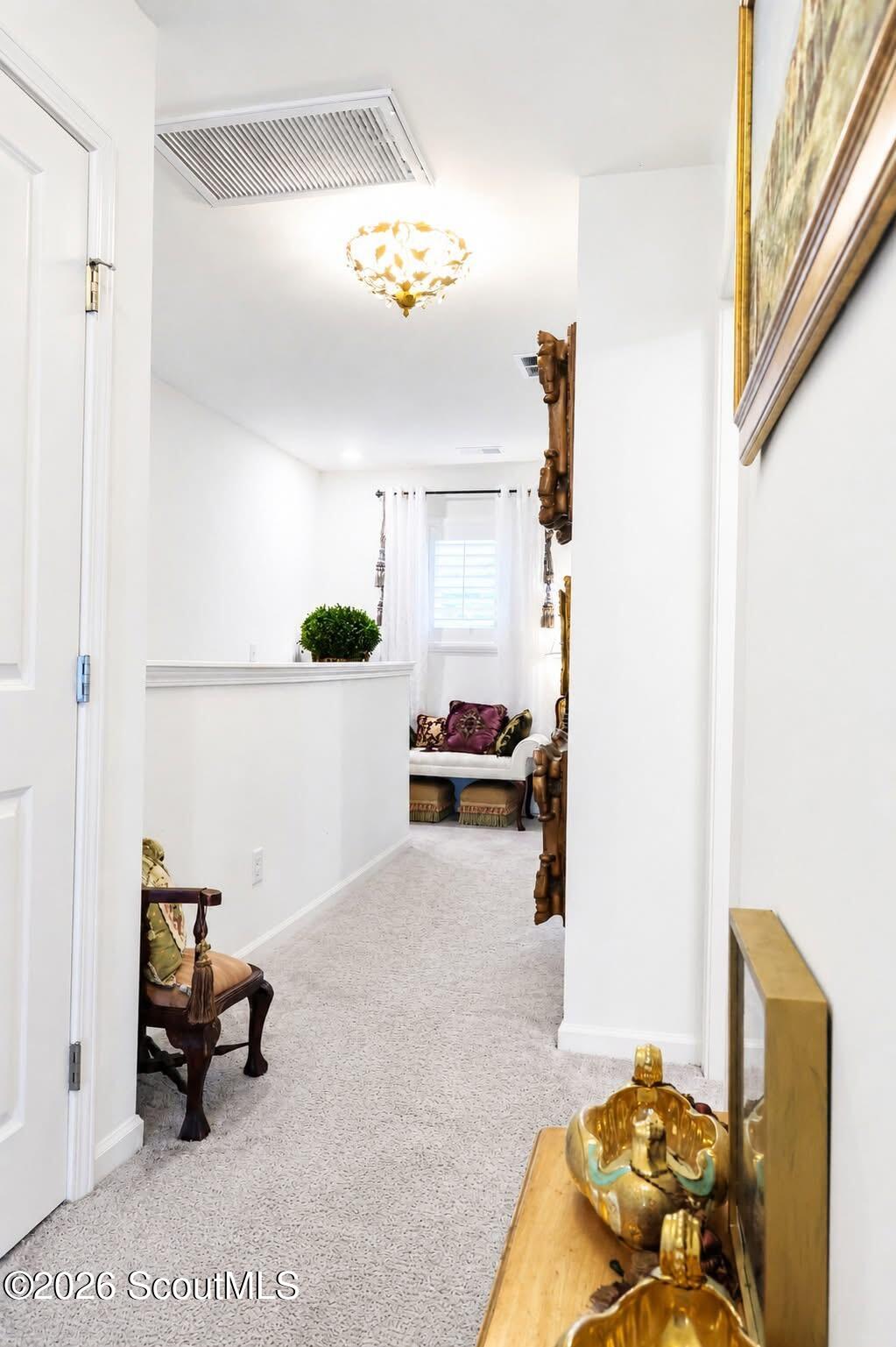 Furnished hallway with pale carpet, a wooden chair, and a white settee at the far end.